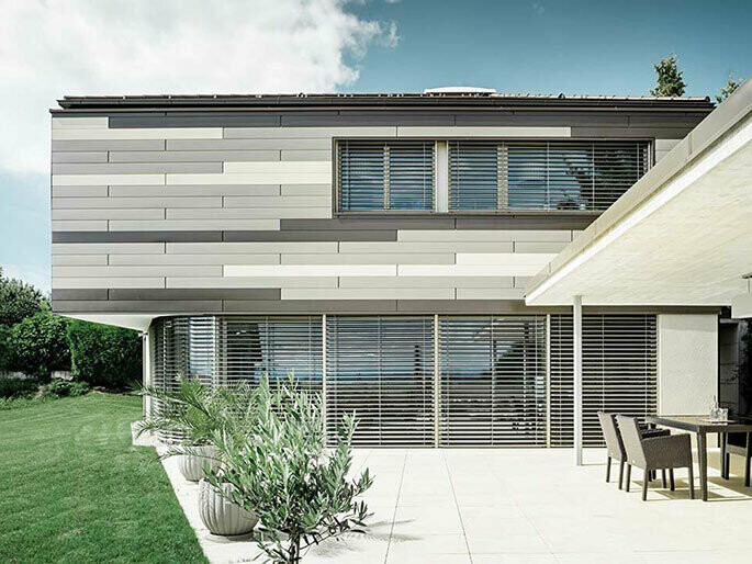Moderne mehrfarbige Fassadengestaltung mit PREFA Sidings in drei Farben mit großen Fensterflächen und großzügiger Terrasse und Flachdach