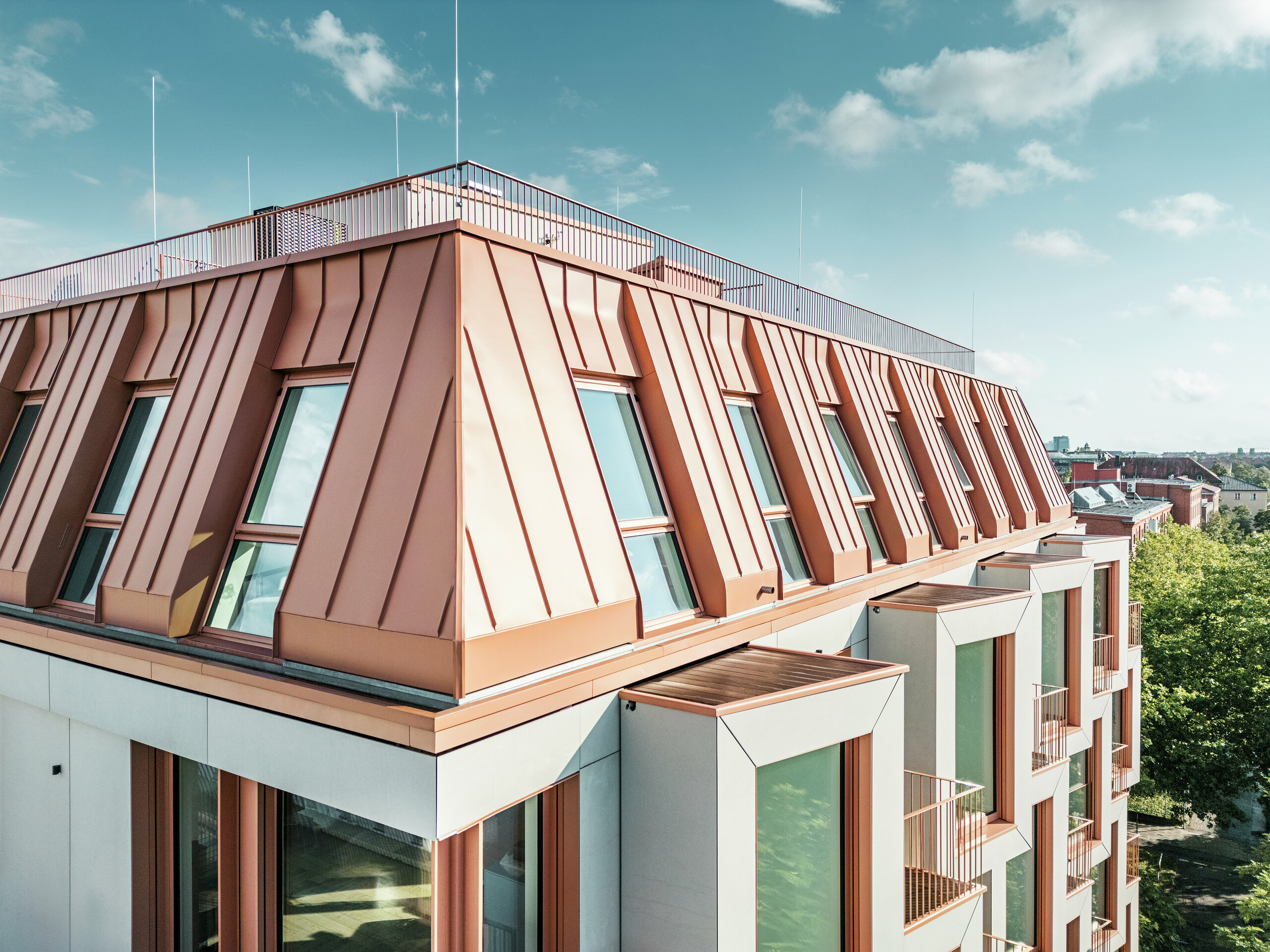 Detailansicht der markanten PREFALZ Dacheindeckung am Wohnhaus Van B in München. Das farblich abgestimmte Aluminiumdach überzeugt durch seine hochwertige Verarbeitung, extreme Langlebigkeit und Witterungsbeständigkeit. Die schräg gestellten Fenster und klar strukturierten Fassadenelemente runden das innovative Designkonzept ab. Ideal für moderne Architektur, bei der Funktionalität und Ästhetik im urbanen Wohnungsbau Hand in Hand gehen. Am unteren Bildrand sind die aneinandergereihten Erker zu sehen.