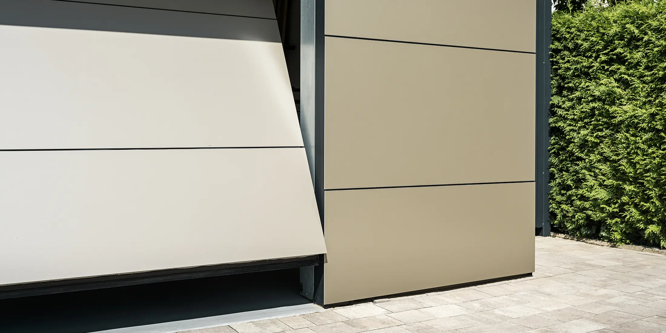 Nahaufnahme eines automatischen Garagentors. Die Garage und das automatische Garagentor sind mit bronzefarbenen Aluminium Verbundplatten verkleidet. Die präzise Verarbeitung spiegelt die Qualität der langlebigen Verbundplatten wider. Der schmale Öffnungsspalt gewährt einen kleinen Einblick in das Innere der Garage.