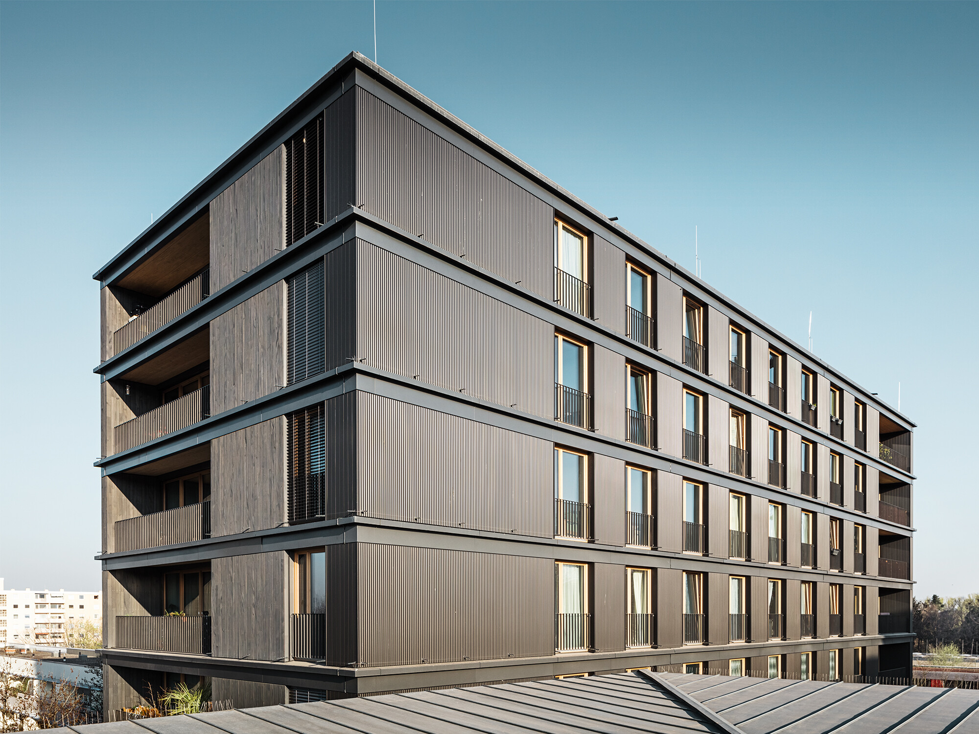 Das Wohn- und Geschäftshaus aus der Seitenperspektive: Die Profilwelle von PREFA und die Holzfassade sind kaum voneinander zu unterscheiden.