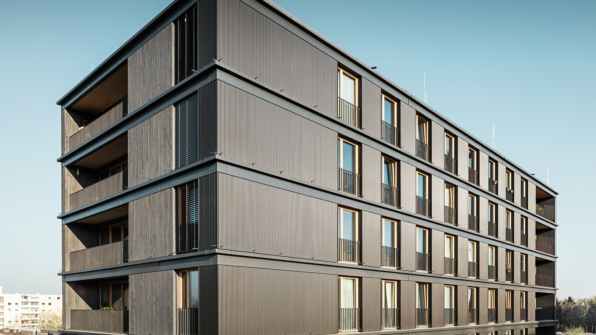 Das Wohn- und Geschäftshaus aus der Seitenperspektive: Die Profilwelle von PREFA und die Holzfassade sind kaum voneinander zu unterscheiden.