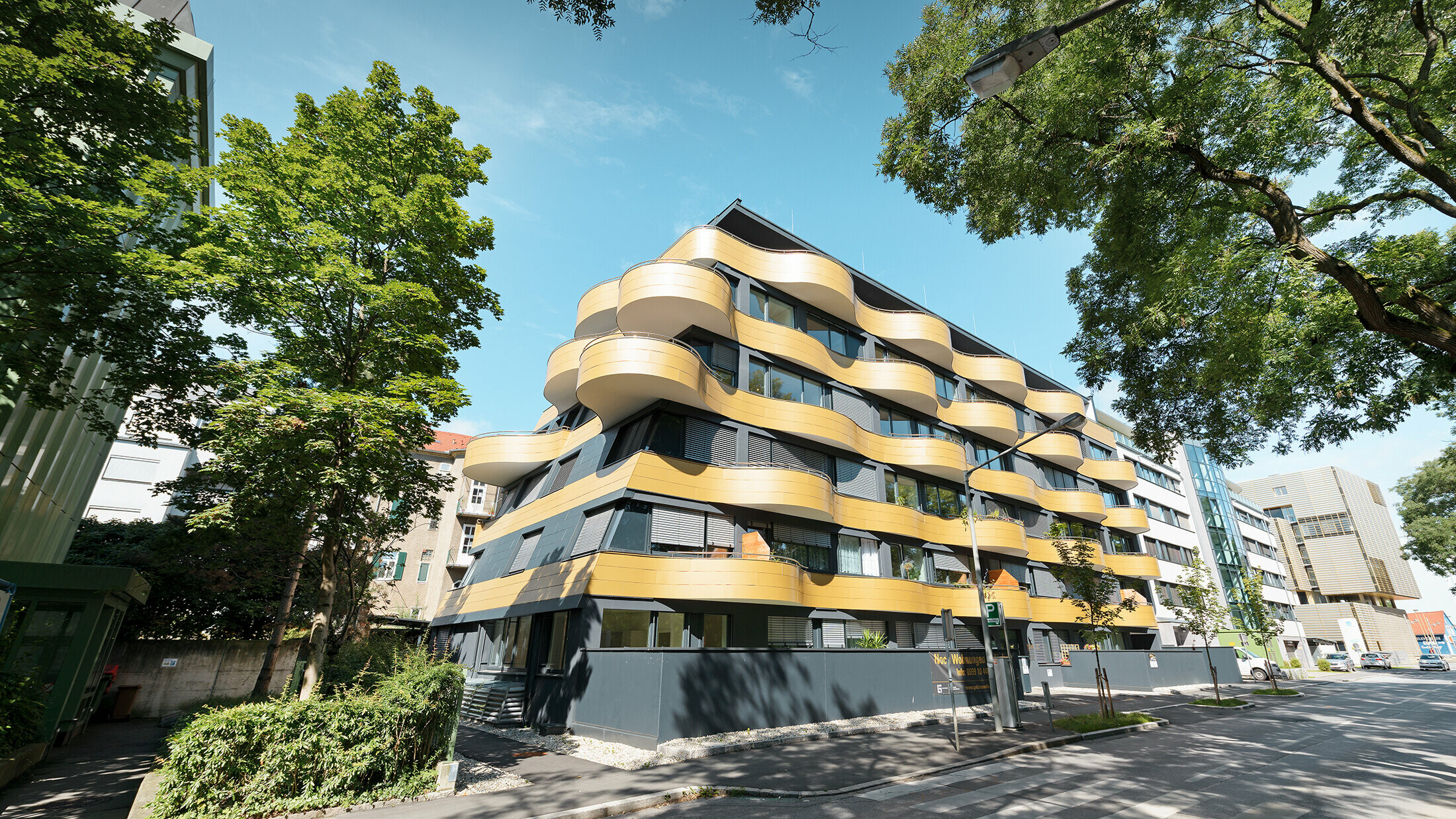 Gesamtansicht der Wohnanlage "Goldene Welle" in Graz, Österreich. Die spektakuläre Fassadengestaltung wurde mit goldfarbenen Aluminium Verbundplatten realisiert. Die runden Balkone sind Wellen nachempfunden.
