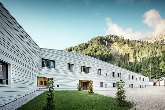 Aluminium trifft Präzision – ein harmonischer Dialog zwischen Technik und Natur. Vor der eindrucksvollen Kulisse der Dolomiten präsentiert sich das „Villaggio Alpino Tempesti“ mit klarer Linienführung und moderner Gestaltung. Die Fassade aus PREFALZ in der Farbe P.10 Prefaweiß ist nicht nur äußerst widerstandsfähig, sondern sorgt durch ihre helle Farbe auch für ein angenehmes Mikroklima, da sie die Sonnenstrahlen reflektiert. Grünflächen und Holzelemente im Eingangsbereich des Militärgebäudes schaffen eine überraschend einladende Atmosphäre.