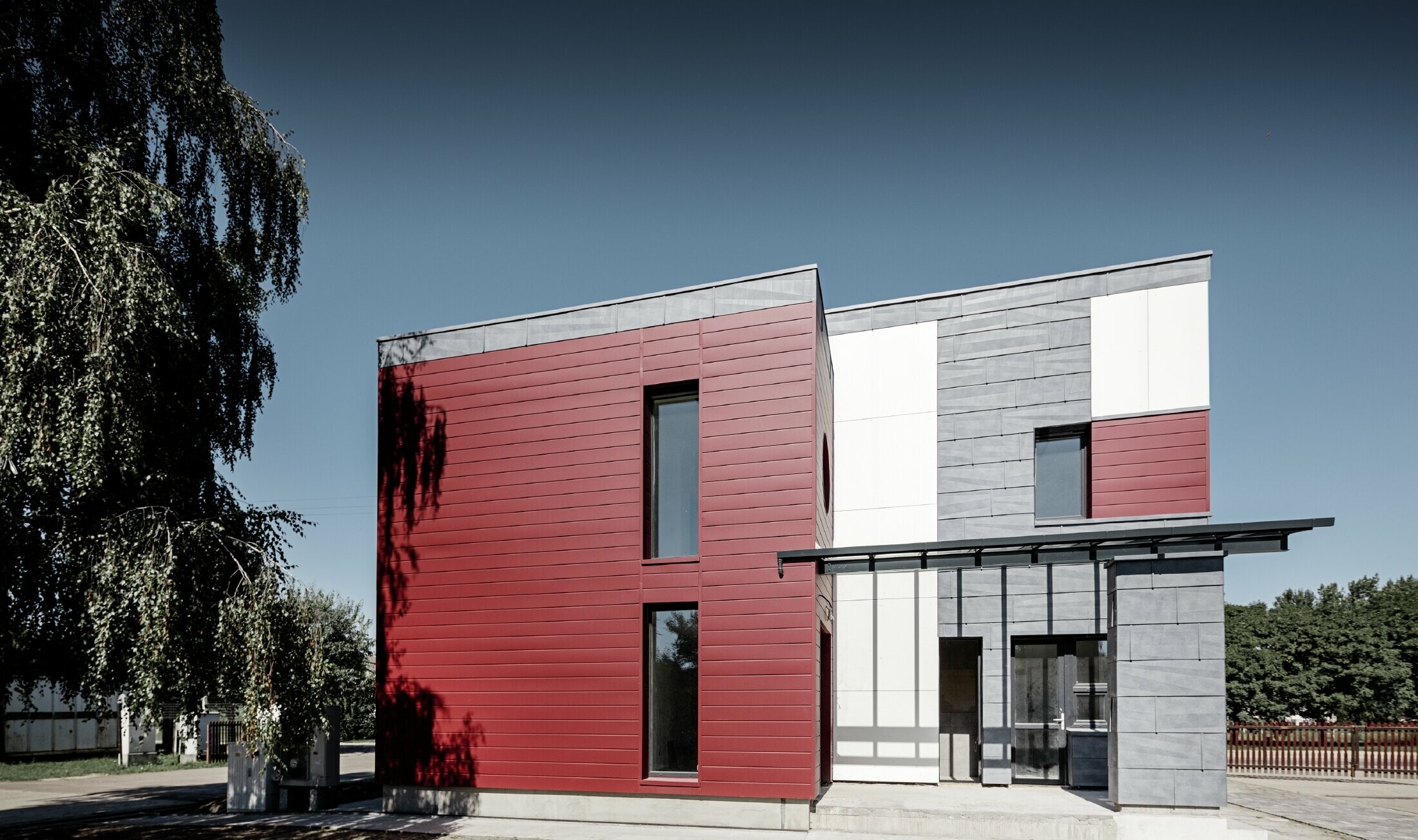 Modernes Bürogebäude mit einer geteilten Fassade in rot, steingrau und weiß mit Aluminiumprodukten Sidings, Fassadenpaneel FX.12 und Aluminium Verbundplatte von PREFA