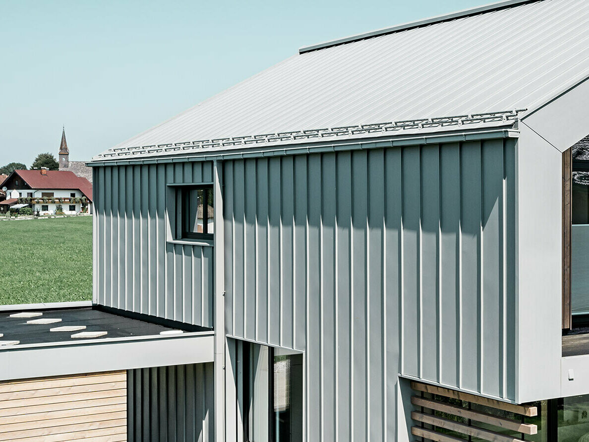Einfamilienhaus mit Satteldach, mit PREFALZ auf Dach und Fassade; Zur Dachentwässerung wird die PREFA Kastenrinne mit dem PREFA Quadratrohr in der Sonderfarbe Patina grau verwendet.