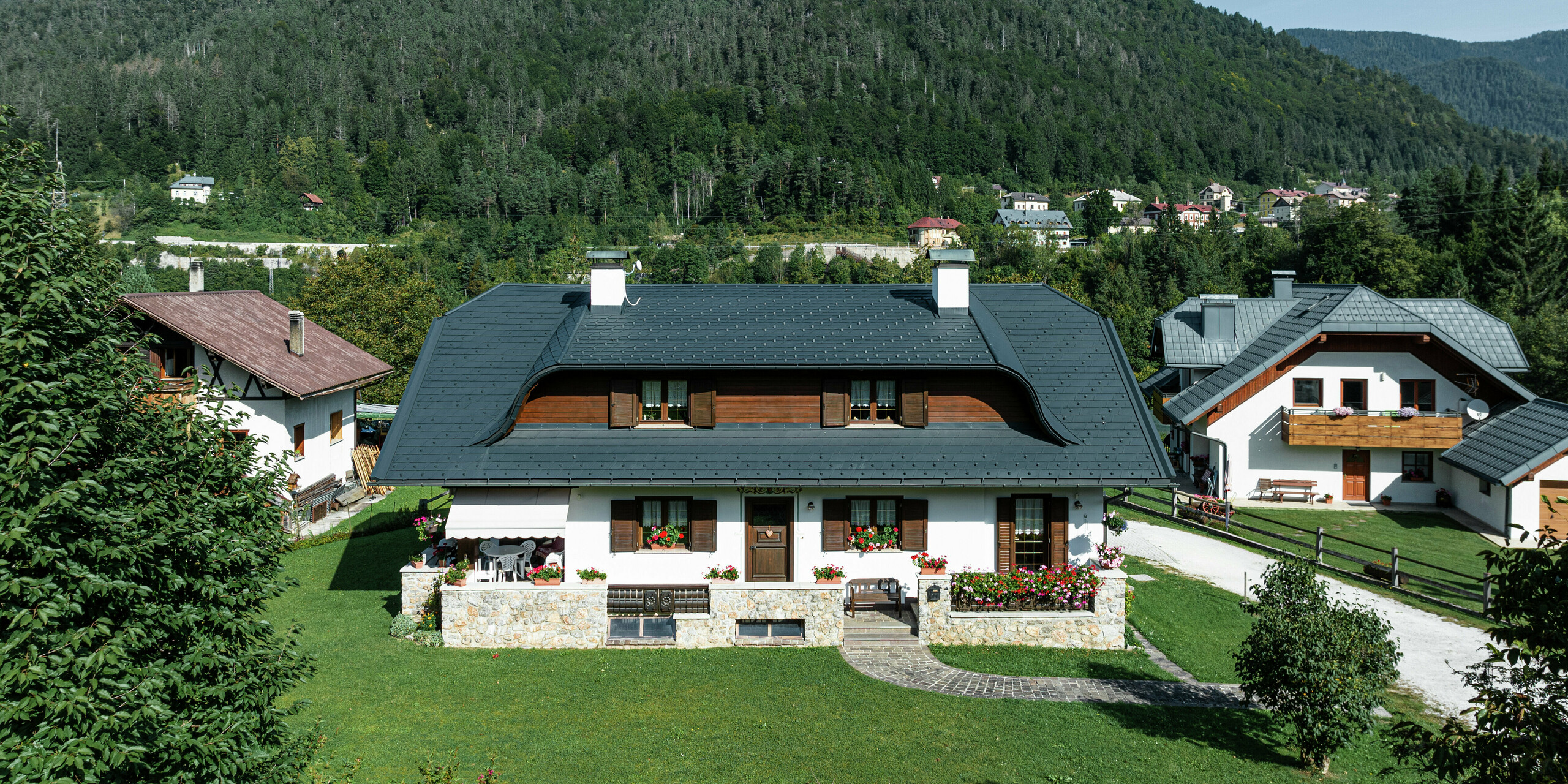 Vor der beeindruckenden Kulisse der italienischen Alpen präsentiert sich dieses sanierte Einfamilienhaus mit einer stilvollen PREFA Dacheindeckung aus hochwertigem Blech. Die markante Hechtgaube verleiht dem Dach eine elegante Dynamik, während die robusten PREFA Dachschindeln in P.10 Anthrazit optimalen Schutz vor Wind und Wetter bieten. Die Kombination aus weißer Fassade, Holzdetails und dunkler Dacheindeckung ergibt ein harmonisches Gesamtbild, das Tradition und Moderne perfekt verbindet.