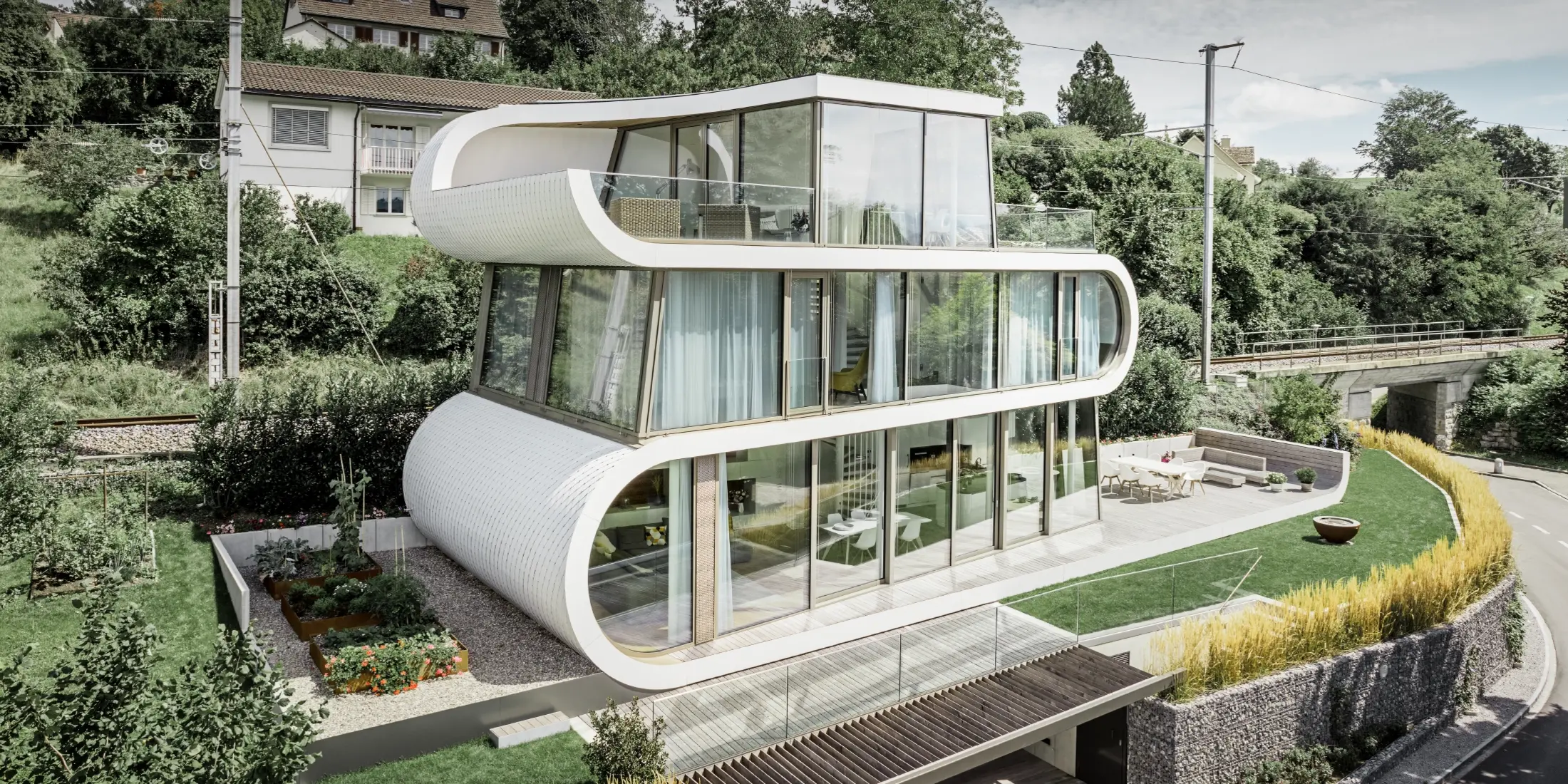 Sehr modernes Einfamilienhaus entworfen durch Architekt Camenzind aus Zürich; Ein geschwungenes Band verbindet die einzelnen Ebenen miteinander. Die Rundungen wurden mit der PREFA Dachraute klein in Reinweiß verkleidet. Das Haus hat viele und große Glasflächen, wodurch das ganze Haus sehr offen wirkt.