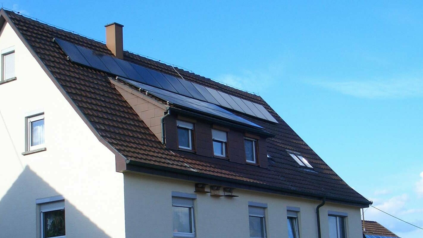 Einfamilienhaus mit sanierungsbedürftigem Ziegeldach; Das Dach hat eine Gaube und eine Photovoltaikanlage.