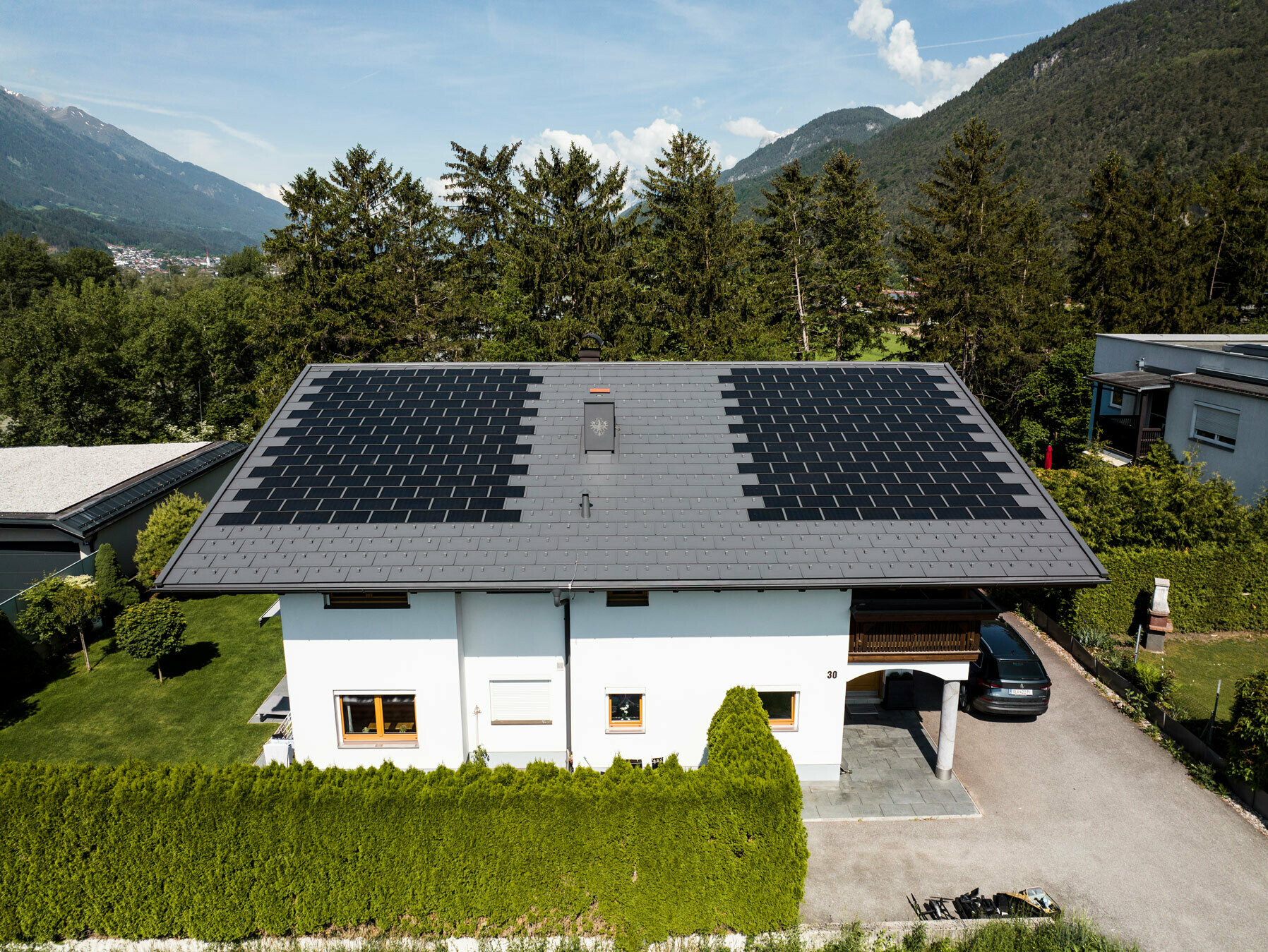 Zu sehen ist ein Einfamilienhaus eingedeckt mit der PREFA Solardachplatte klein mit Dachplatte R.16 in der Farbe P.10 Dunkelgrau in ländlicher Umgebung.