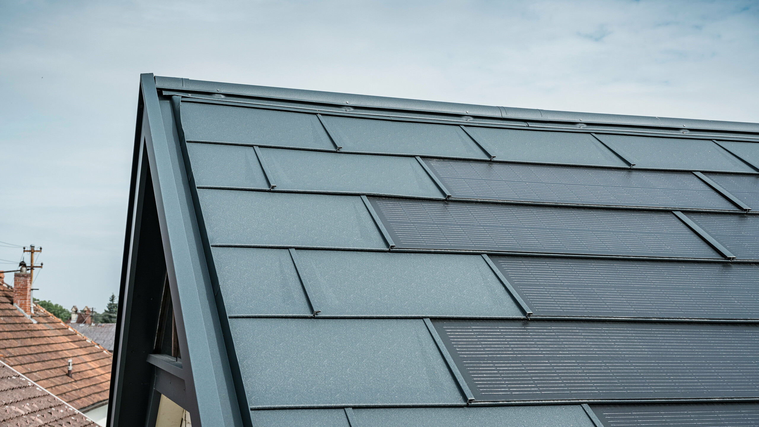 Detailansicht eines Hausdachs ausgestattet mit der innovativen PREFA Solardachplatte. Die Dachplatten mit integrierten Photovoltaikzellen präsentieren sich in einem eleganten Anthrazit. Die homogene Oberfläche fügt sich nahtlos in das Dach ein und sorgt damit für eine moderne und saubere Optik. Das innovative Dachsystem schafft eine effiziente Energienutzung ohne Beeinträchtigung der Ästhetik.