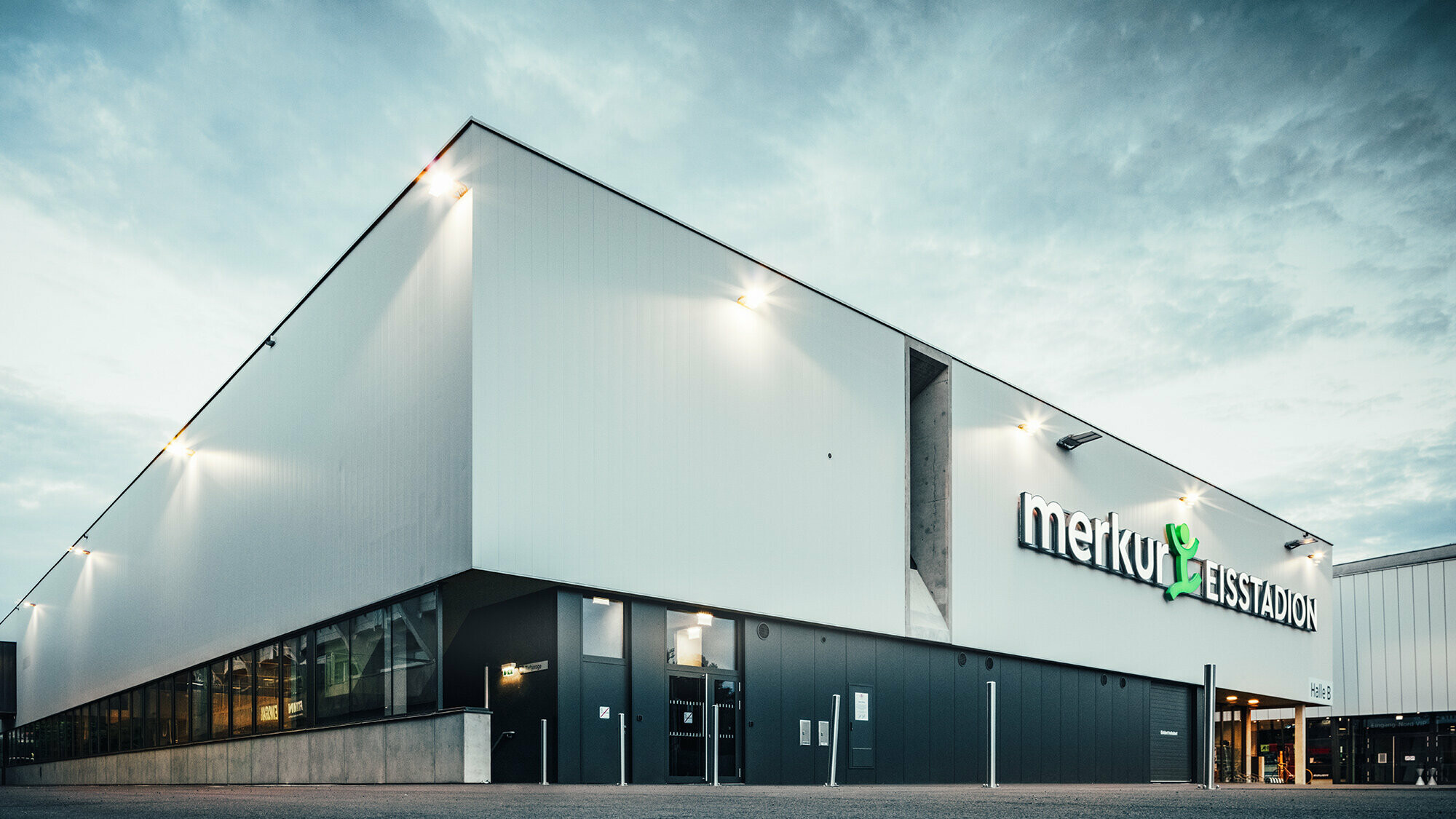 Eckaufnahme der Eishalle. An der rechten Seitenwand zu sehen: Lüftungsschacht und die Aufschrift "merkur EISSTADION" an der Fassade.