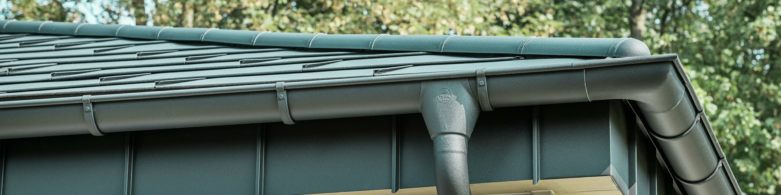 Detailansicht der PREFA Dachentwässerung eines Bungalows in Rommerskirchen. Die hochwertige Saumrinne und das Ablaufrohr in P.10 Schwarz bieten eine sichere Dachentwässerung bei Regen. Die langlebigen PREFA Aluminiumprodukte verbinden Funktionalität mit modernem, elegantem Design.