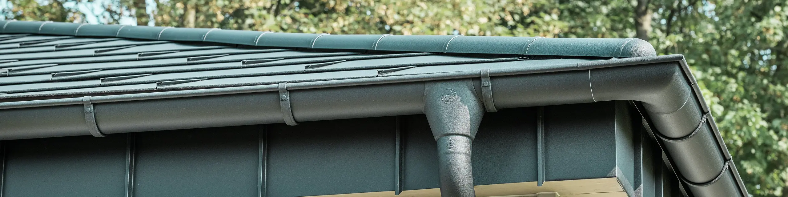 Detailansicht der PREFA Dachentwässerung eines Bungalows in Rommerskirchen. Die hochwertige Saumrinne und das Ablaufrohr in P.10 Schwarz bieten eine sichere Dachentwässerung bei Regen. Die langlebigen PREFA Aluminiumprodukte verbinden Funktionalität mit modernem, elegantem Design.
