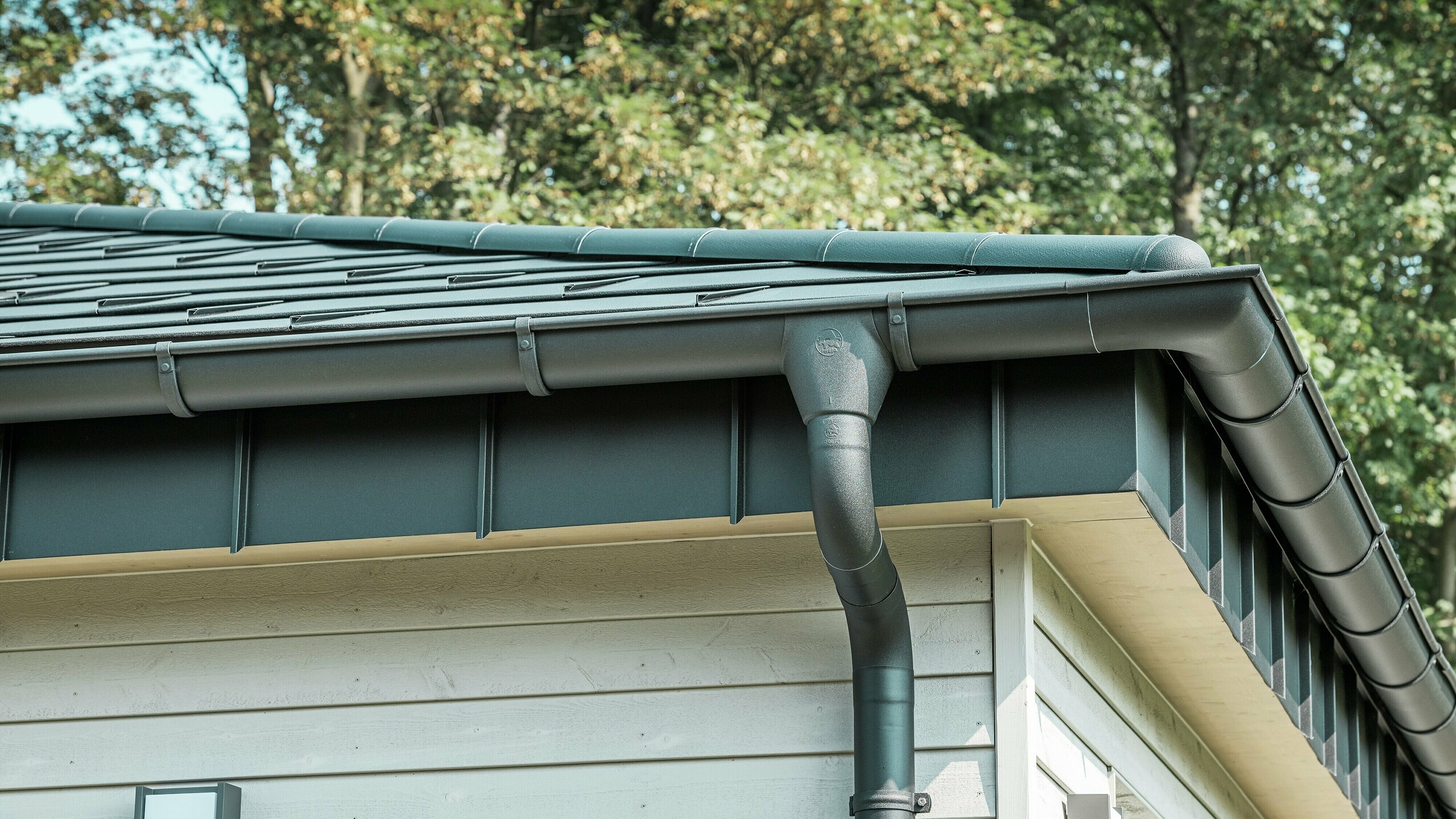 Detailansicht der PREFA Dachentwässerung eines Bungalows in Rommerskirchen. Die hochwertige Saumrinne und das Ablaufrohr in P.10 Schwarz bieten eine sichere Dachentwässerung bei Regen. Die langlebigen PREFA Aluminiumprodukte verbinden Funktionalität mit modernem, elegantem Design.