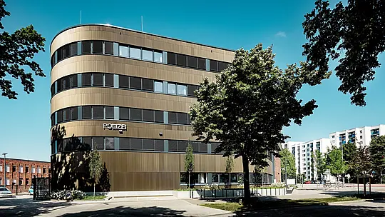 Dynamische Architekturaufnahme des Polizeikommissariats 43 in Hamburg: Der geschwungene Neubau mit PREFA Aluminiumfassade aus Strangpressprofilen „Zacke“ in Mittelbronze zieht als markanter Eyecatcher im Stadtbild alle Blicke auf sich. Die fein strukturierte Oberfläche erzeugt lebendige Licht- und Schatteneffekte zwischen horizontalen Fensterbändern und betont die fließenden Linien der Fassade. PREFA Aluminium überzeugt durch hohe Korrosionsbeständigkeit, Langlebigkeit und geringen Wartungsaufwand – ideal für nachhaltige, funktionale und architektonisch präzise Fassadenlösungen.