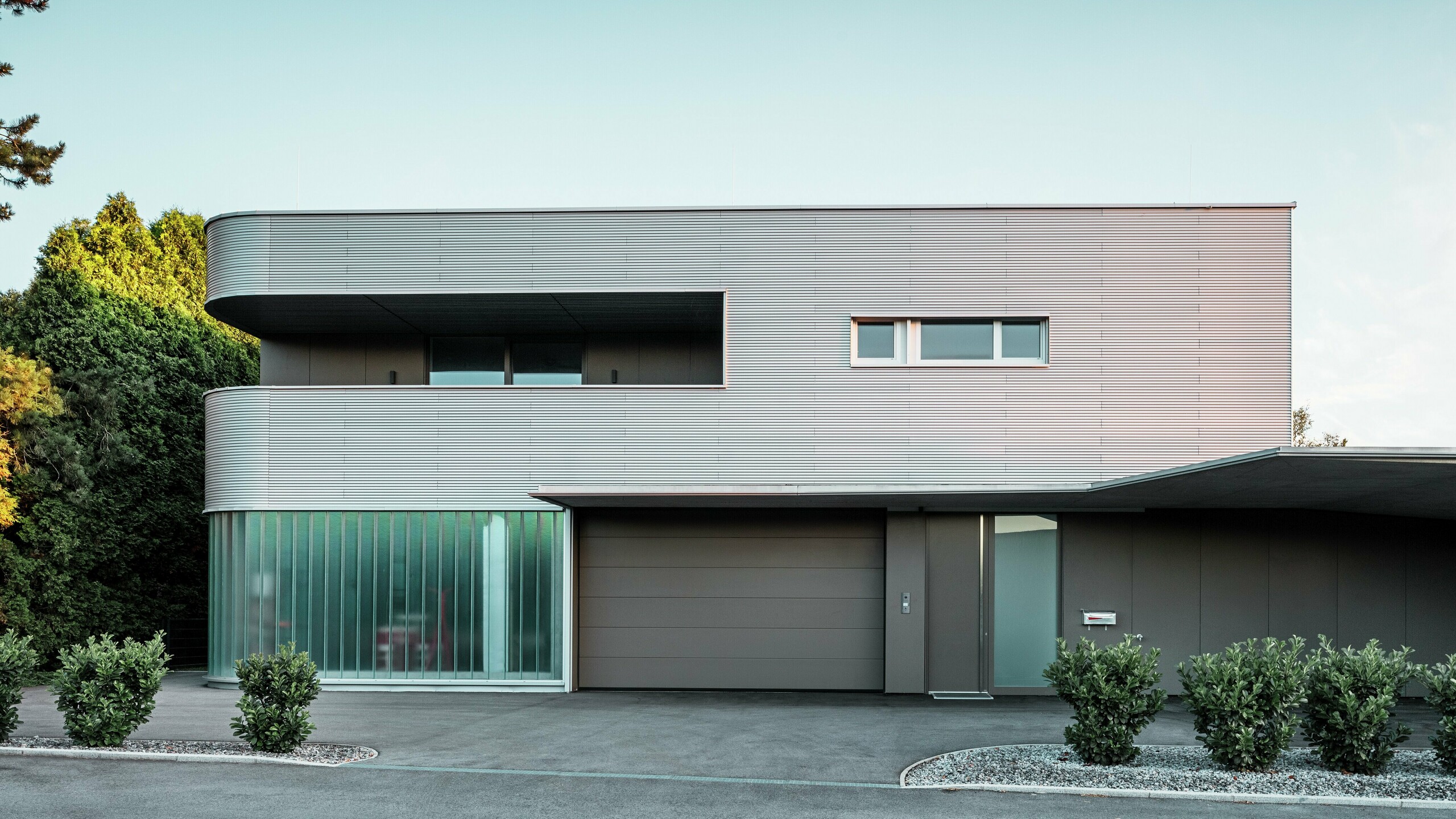 Modernes Wohnhaus mit naturblanker Fassade aus der PREFA Profilwelle mit Garage bei Tageslicht.