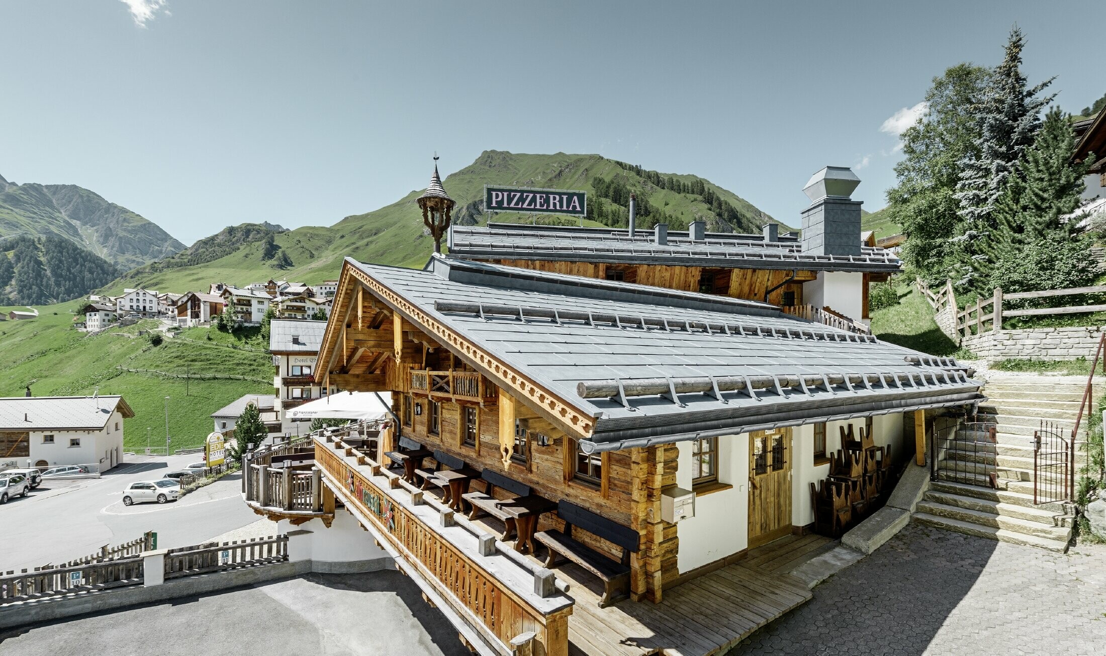 Restaurant Almrausch mit Bergen im Hintergrund und einem PREFA Dach mit dem Dachpaneel FX.12 in steingrau und Gebirgsschneestützen