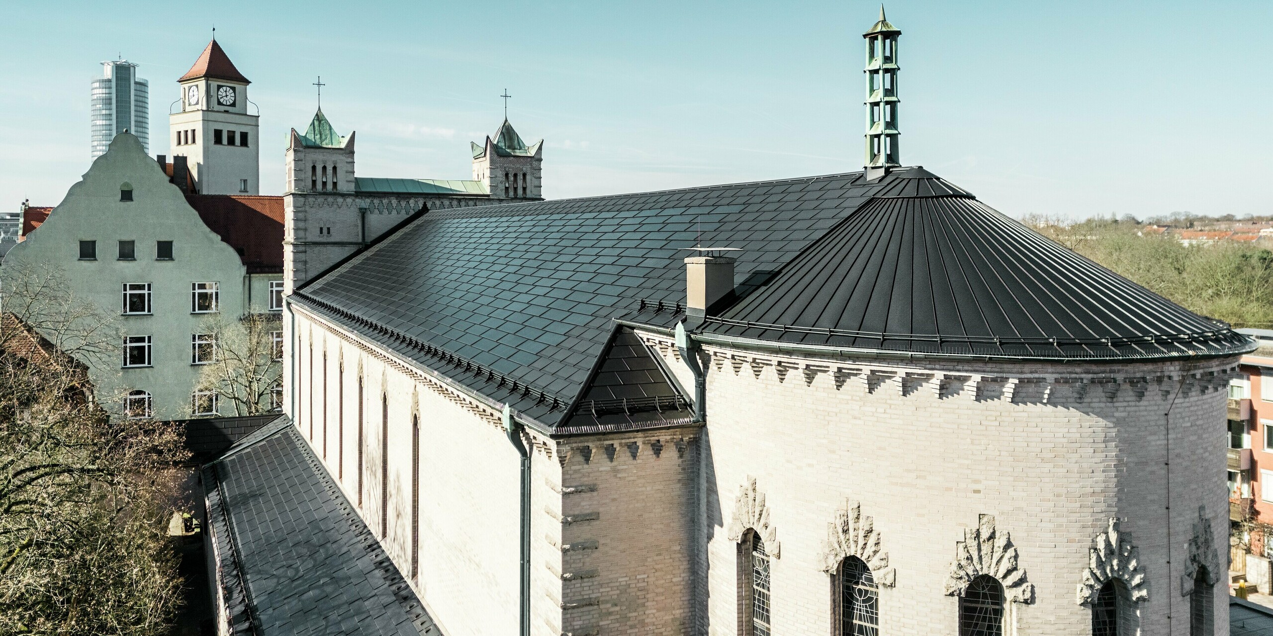 Die Sanierung der St. Karl Borromäus Kirche in Nürnberg zeigt eindrucksvoll, wie sich moderne PREFA Solardachplatten harmonisch in den Denkmalschutz integrieren lassen. Auf dem Dach ermöglichen die schwarzen Solardachplatten eine effiziente und umweltfreundliche Stromerzeugung. Nebengebäude der Kirche wurden mit der PREFA Dachplatte R.16 eingedeckt. Die beeindruckende Rundung auf der Gebäuderückseite wurde mit einer Aluminium-Stehfalzdeckung verkleidet.