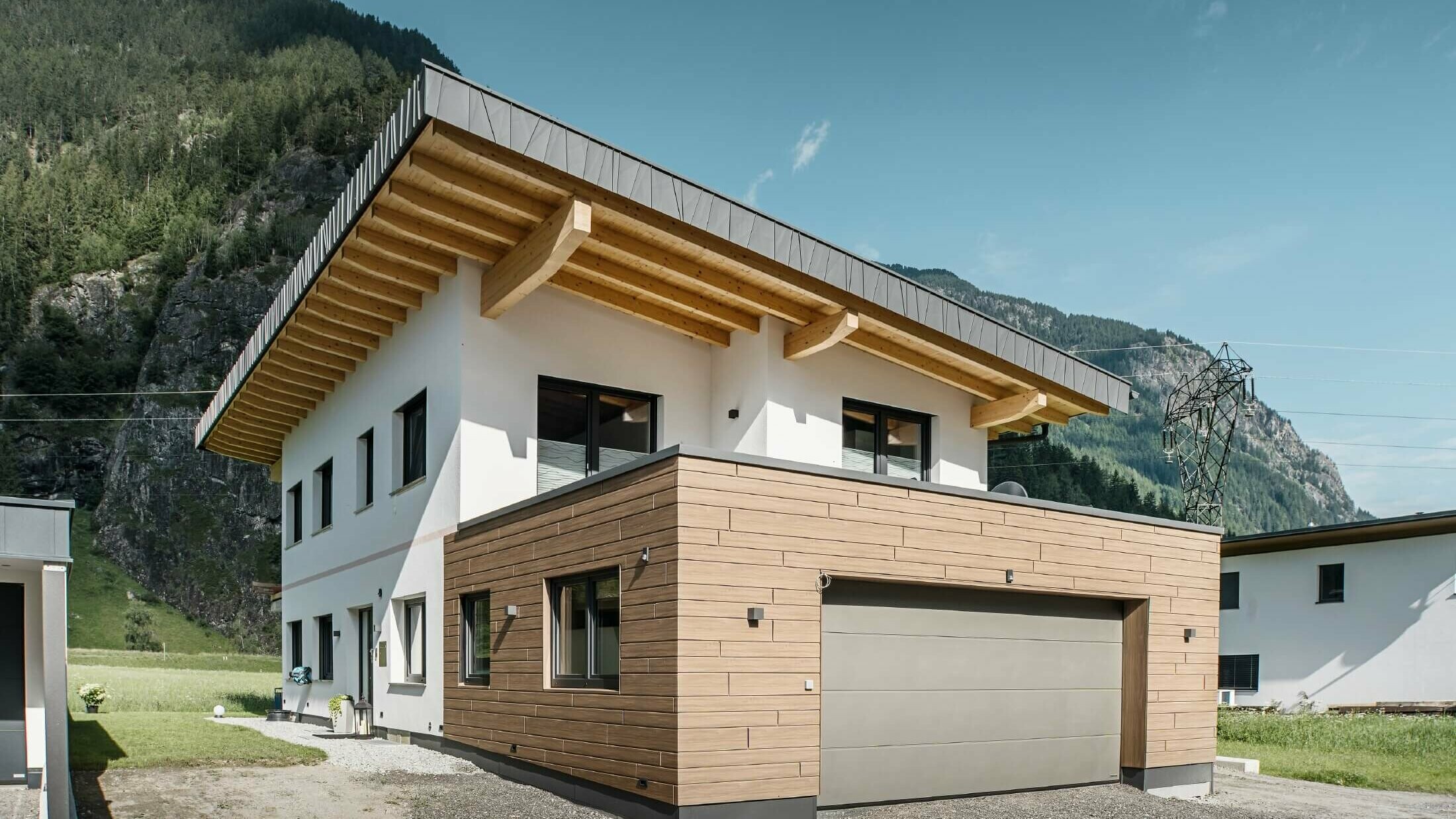 Garage eines Wohnhauses mit PREFA Sidings in Holzoptik im Farbton "Walnuss Braun". Im Hintergrund sind Berge zu sehen. 