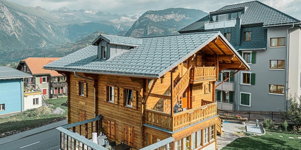 Traditionelles Schweizer Holzchalet mit Gaube und Satteldach; Das Dach ist mit den klassischen PREFA Dachplatten in Steingrau eingedeckt.