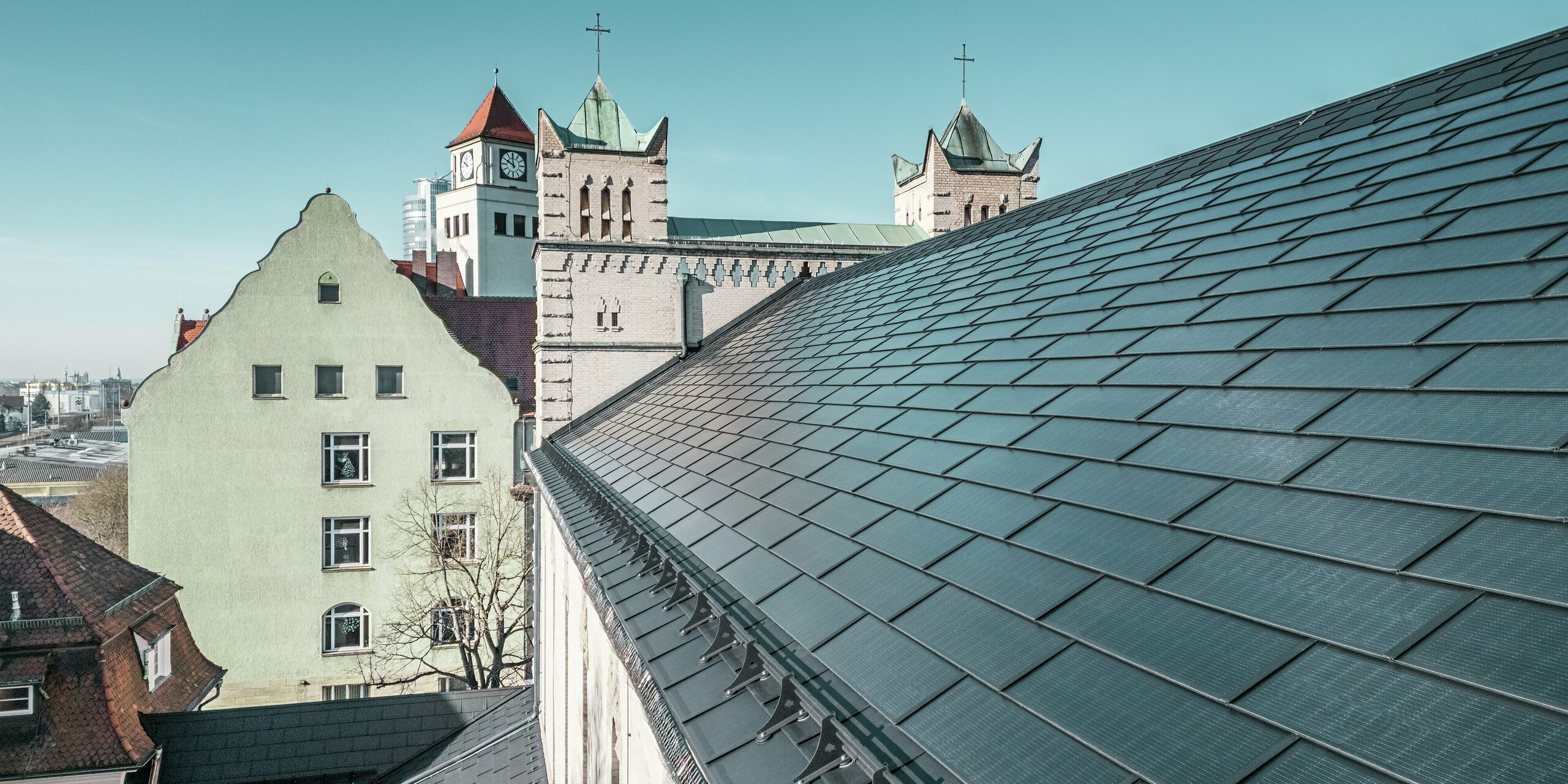 Die Nahaufnahme des Daches der St. Karl Borromäus Kirche in Nürnberg zeigt die präzise verlegten PREFA Solardachplatten in elegantem Schwarz. Die gut integrierten Solarmodule fügen sich harmonisch in die historische Architektur ein und stellen eine nachhaltige Energiequelle dar. Im Hintergrund sind die markanten Kirchtürme mit ihren klassischen spitzen Dächern zu sehen. Die PREFA Dachlösung aus robustem Aluminium verbindet Denkmalschutz mit erneuerbarer Energie perfekt.