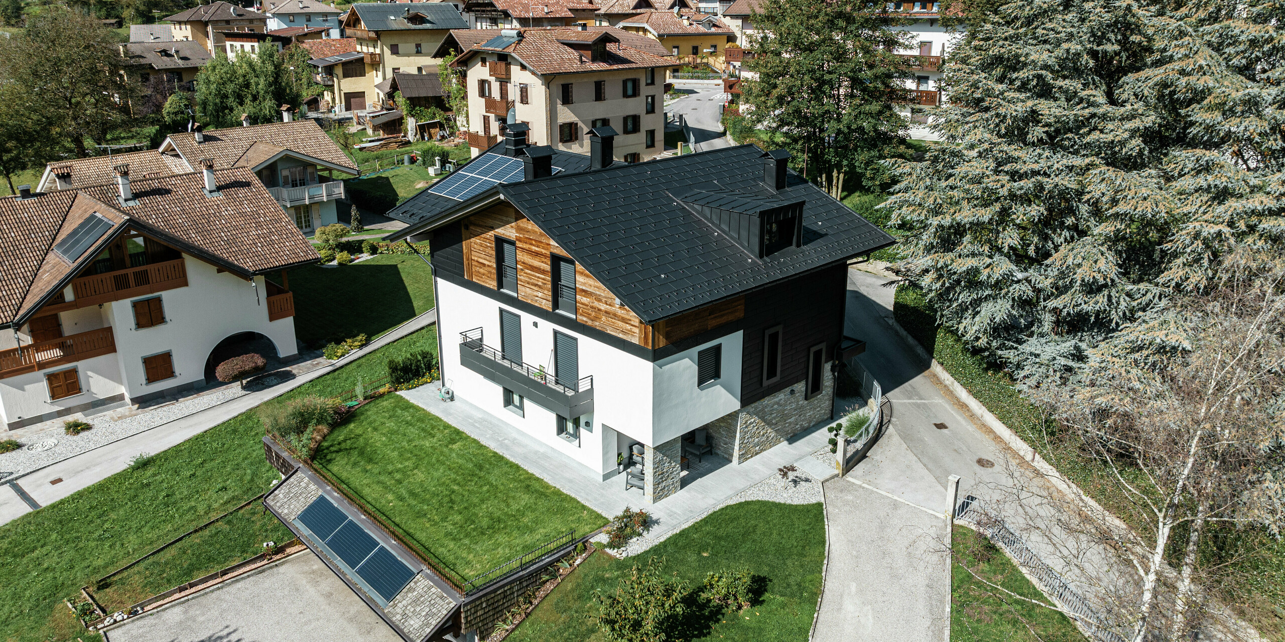 Vogelperspektive auf ein modern renoviertes Wohnhaus in Pelugo, Italien, mit PREFA Dachplatten R.16 in P.10 Anthrazit und PREFA Siding.X Fassadenpaneelen. Die Kombination von Aluminium, Holz und Stein sorgt für eine harmonische, witterungsbeständige und nachhaltige Architektur.