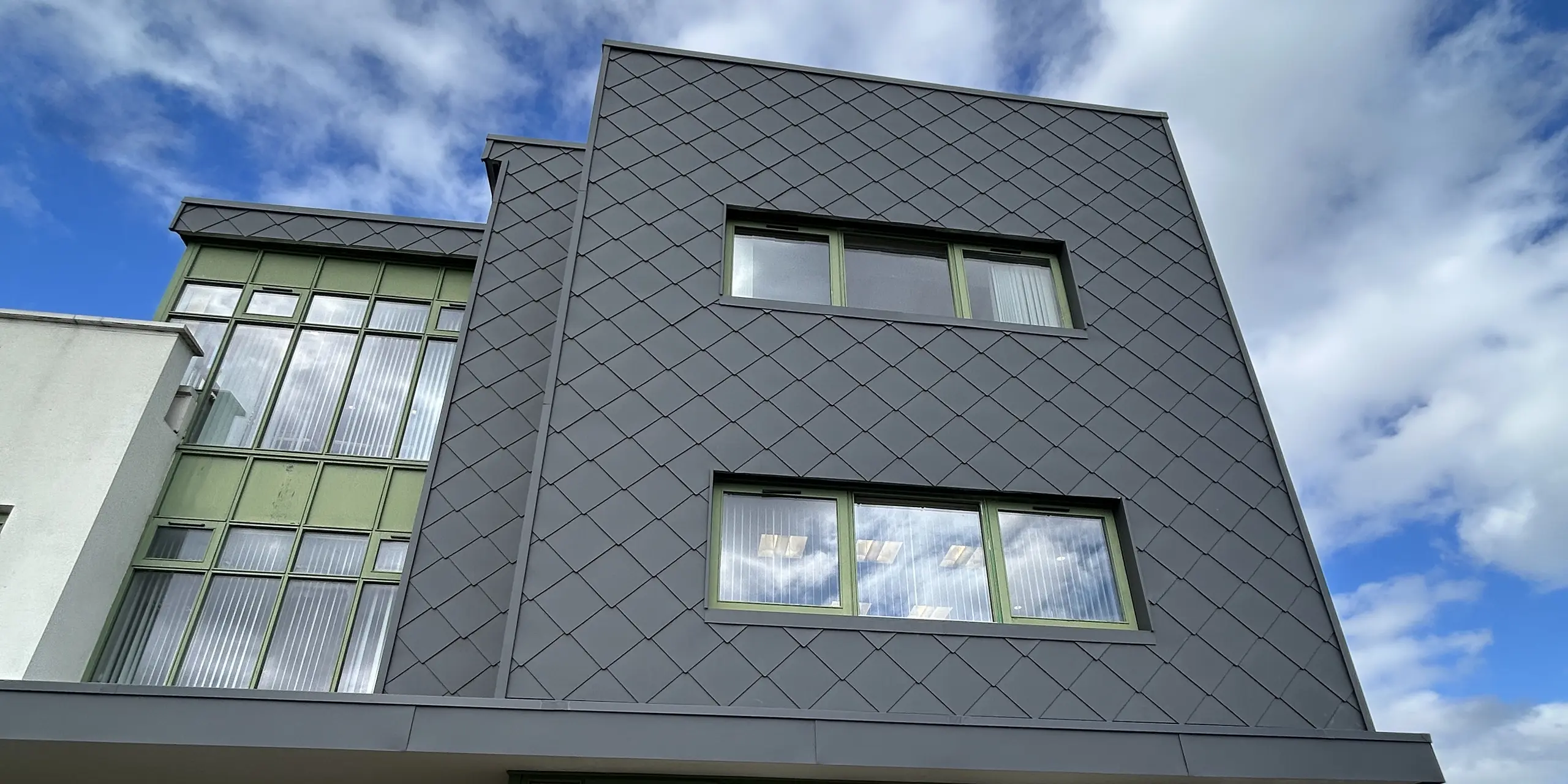 Die moderne Gebäudefassade des CAHMS Centres in Wexford wurde mit PREFA Wandraute 44 x 44 in der Farbe P.10 Dunkelgrau verkleidet. Die markante Rautenstruktur erzeugt lebendige Licht- und Schatteneffekte, während die grün gerahmten Fenster frische Kontraste setzen. Die langlebige Aluminiumfassade überzeugt durch ihre hohe Witterungsbeständigkeit, ihren Korrosionsschutz und ihren minimalen Wartungsaufwand.