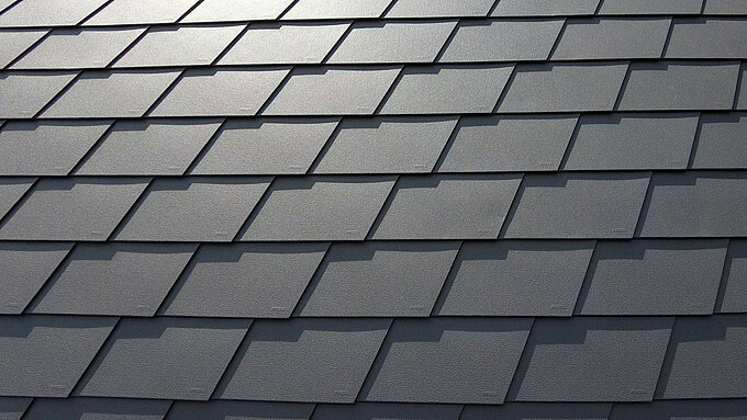 Detailaufnahme einer Dacheindeckung mit PREFA Dachschindeln in P.10 Dunkelgrau. Die Schindeln sind gleichmäßig angeordnet und zeigen die markante, wetterbeständige Aluminiumoberfläche, die eine matte und strukturierte Optik bietet.
