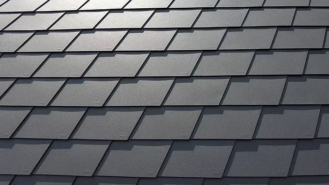 Detailaufnahme einer Dacheindeckung mit PREFA Dachschindeln in P.10 Dunkelgrau. Die Schindeln sind gleichmäßig angeordnet und zeigen die markante, wetterbeständige Aluminiumoberfläche, die eine matte und strukturierte Optik bietet.