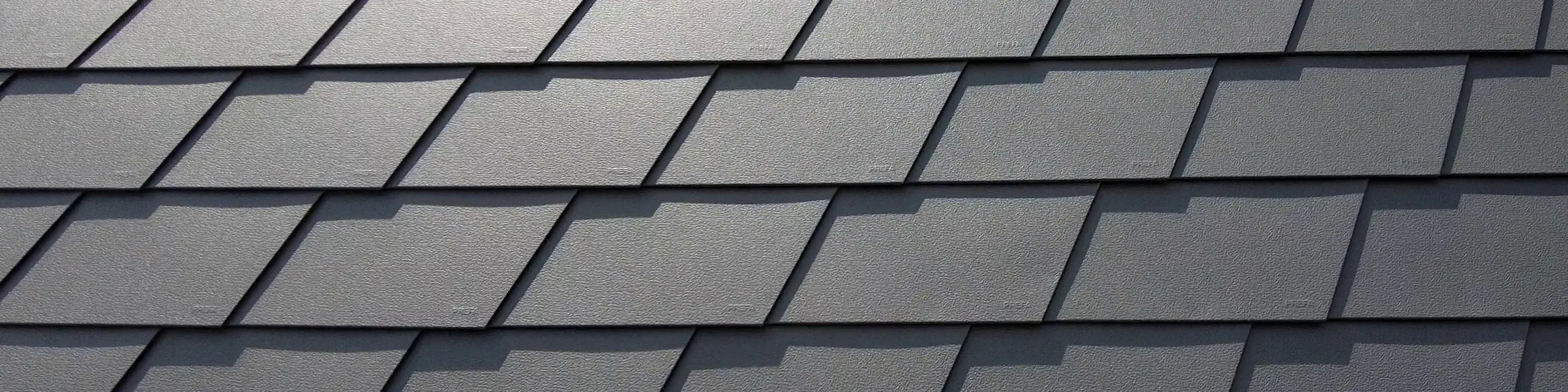 Detailaufnahme einer Dacheindeckung mit PREFA Dachschindeln in P.10 Dunkelgrau. Die Schindeln sind gleichmäßig angeordnet und zeigen die markante, wetterbeständige Aluminiumoberfläche, die eine matte und strukturierte Optik bietet.