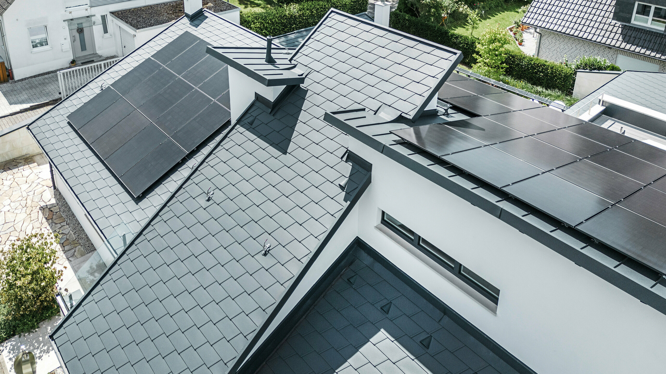Vogelperspektive auf die unterschiedlichen Ebenen am Dach eines modernen Einfamilienhauses in Dortmund wurden mit PREFA Dachschindeln DS.19 und PREFALZ in der Farbe P.10 Anthrazit sowie einer großflächigen PV-Anlage ausgestattet.