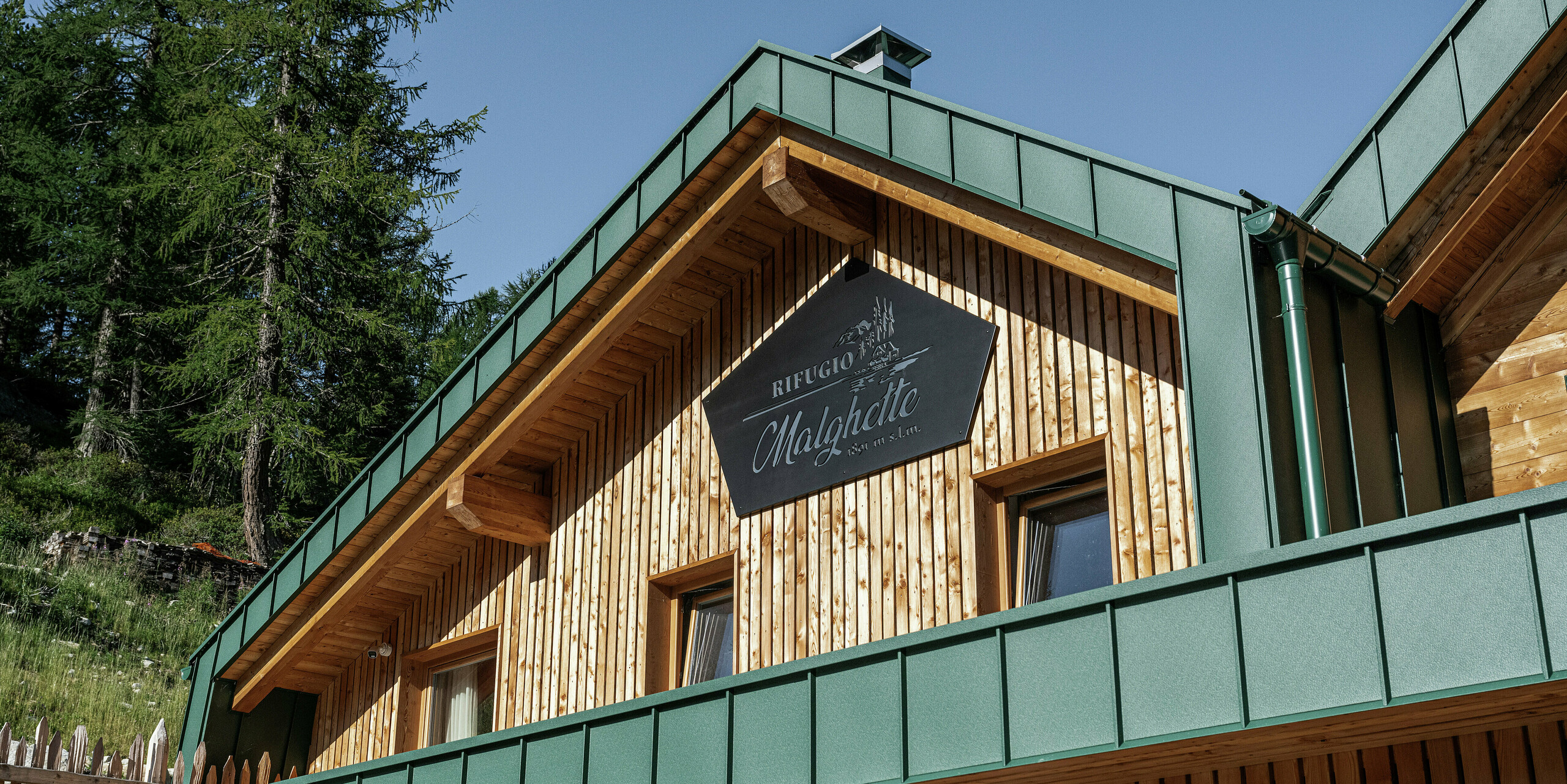 Detailansicht der Fassade des Rifugio Malghette mit PREFALZ in P.10 Moosgrün - widerstandsfähig, wartungsfrei und perfekt kombiniert mit Naturholz. Die langlebige Aluminiumverkleidung schützt die Hütte zuverlässig vor den extremen Witterungsbedingungen in alpiner Höhe.