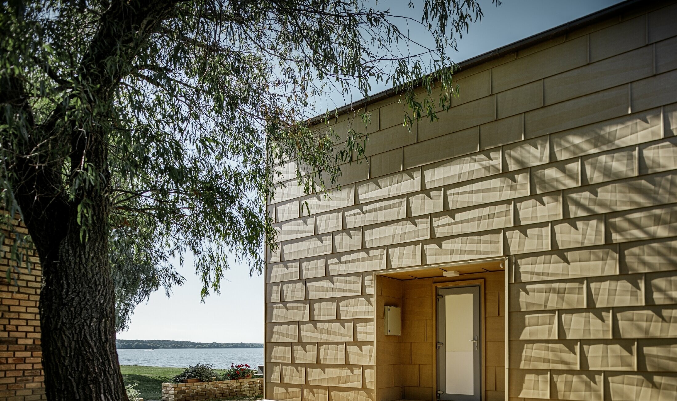 modernes Wochenendhaus mit Flachdach und großen Fensterflächen am See mit einer gekanteten Aluminiumfassade in sandbraun