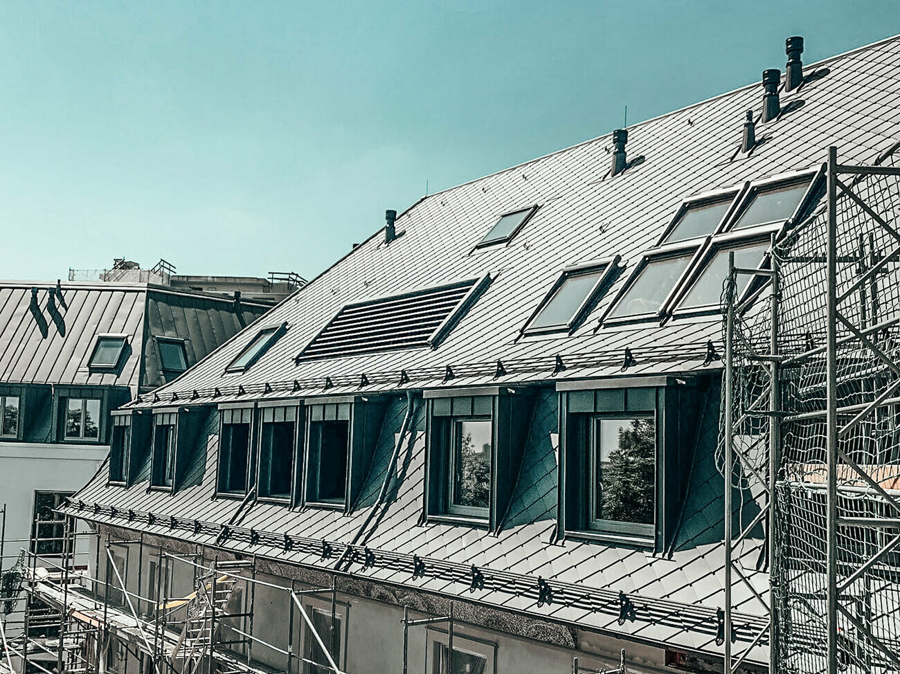 Eine Aufnahme des Daches des Wohnkomplexes Marie. Zu sehen sind die rautenförmigen PREFA-Fassadenziegel 29x29 in P.10 dunkelgrau.