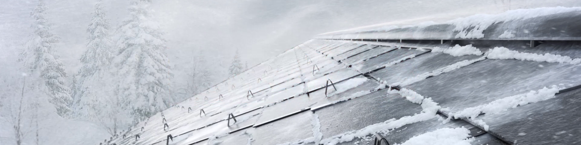 Frühjahrskampagne 2026 von PREFA – Ein schneebedecktes Dach mit Aluminiumplatten, das in einem winterlichen Sturm steht. Im Hintergrund sind verschneite Bäume sichtbar. Die Platten sind mit Schneerändern bedeckt, und die Dachrinnen sind teilweise von Schnee umgeben.