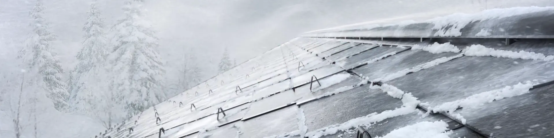 Frühjahrskampagne 2026 von PREFA – Ein schneebedecktes Dach mit Aluminiumplatten, das in einem winterlichen Sturm steht. Im Hintergrund sind verschneite Bäume sichtbar. Die Platten sind mit Schneerändern bedeckt, und die Dachrinnen sind teilweise von Schnee umgeben.