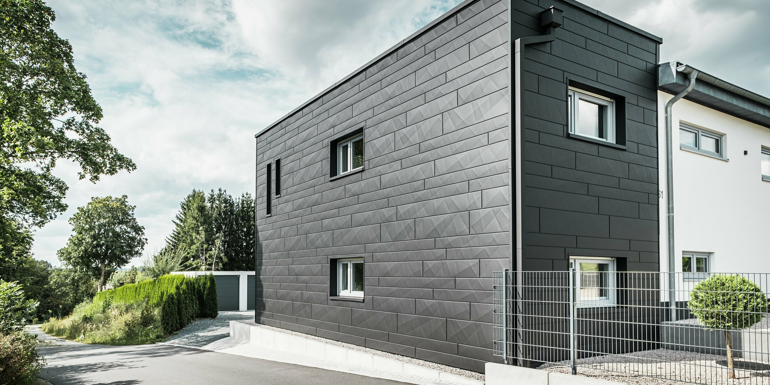 Die Rückseite des modernisierten Einfamilienhauses in Teuschnitz beeindruckt mit einer eleganten Fassade aus PREFA Siding.X in der Farbe P.10 Schwarz. Die geometrischen Blechpaneele erzeugen eine markante, strukturierte Optik und verleihen dem Gebäude einen modernen und zeitlosen Charakter. Die integrierte PREFA Dachentwässerung mit Quadratrohr und Wasserfangkasten fügt sich harmonisch in das Gesamtbild ein und verbindet Ästhetik mit Funktionalität.
