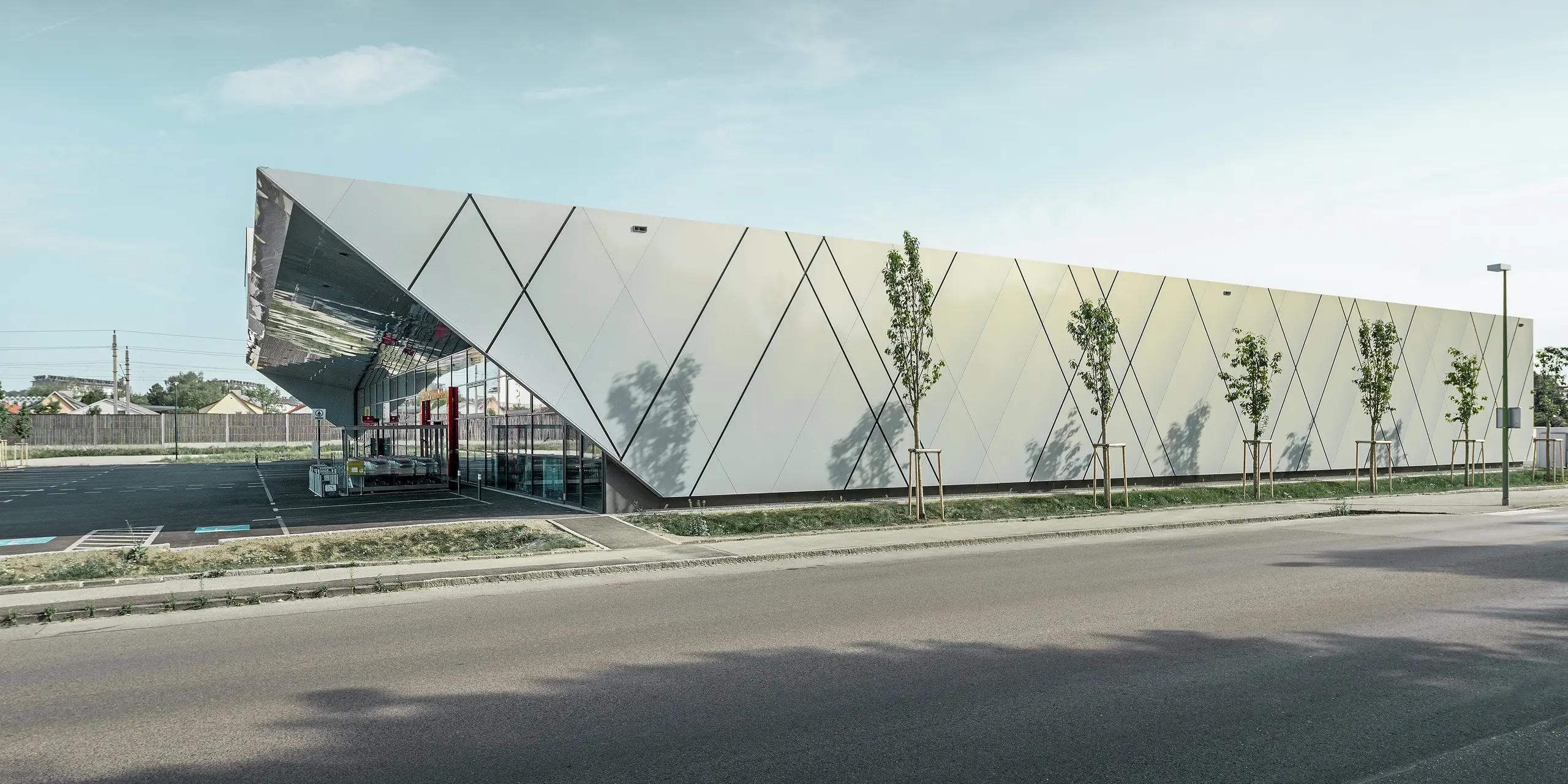 Die Seitenansicht der EUROSPAR Filiale in Wels Gartenstadt zeigt die moderne Fassadengestaltung mit PREFA Aluminium Verbundplatten in der exklusiven Sonderfarbe Silver Gold. Das diagonale Fugenbild verleiht dem Gebäude eine elegante und dynamische Wirkung.