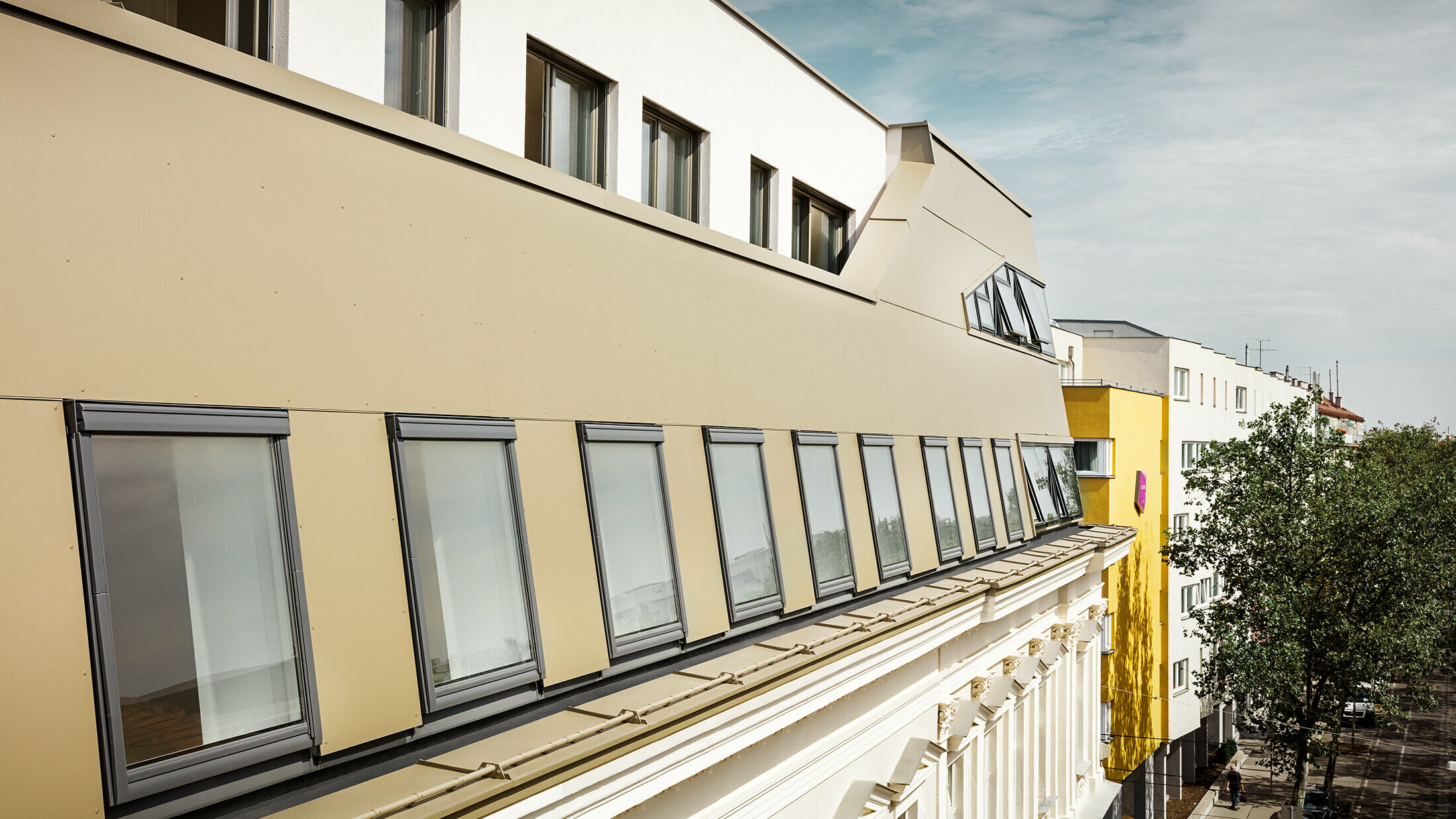 Die seitliche Ansicht des Dachgeschosses hebt die gleichmäßige Verkleidung mit PREFA Aluminium Verbundplatten in Bronze hervor. Große Fenster und flächige Glaselemente sorgen für lichtdurchflutete Räume und ein elegantes, modernes Erscheinungsbild.