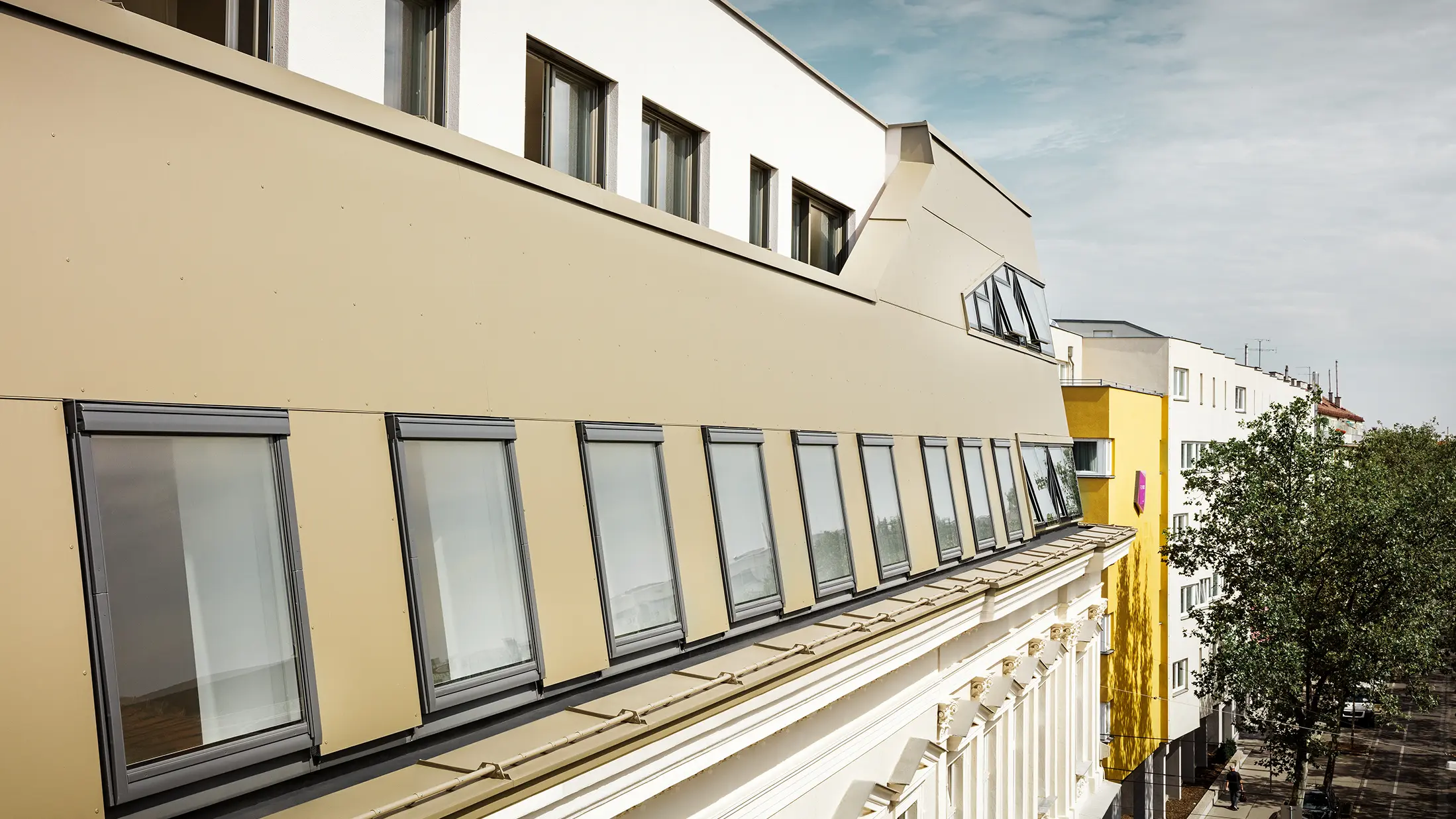 Die seitliche Ansicht des Dachgeschosses hebt die gleichmäßige Verkleidung mit PREFA Aluminium Verbundplatten in Bronze hervor. Große Fenster und flächige Glaselemente sorgen für lichtdurchflutete Räume und ein elegantes, modernes Erscheinungsbild.