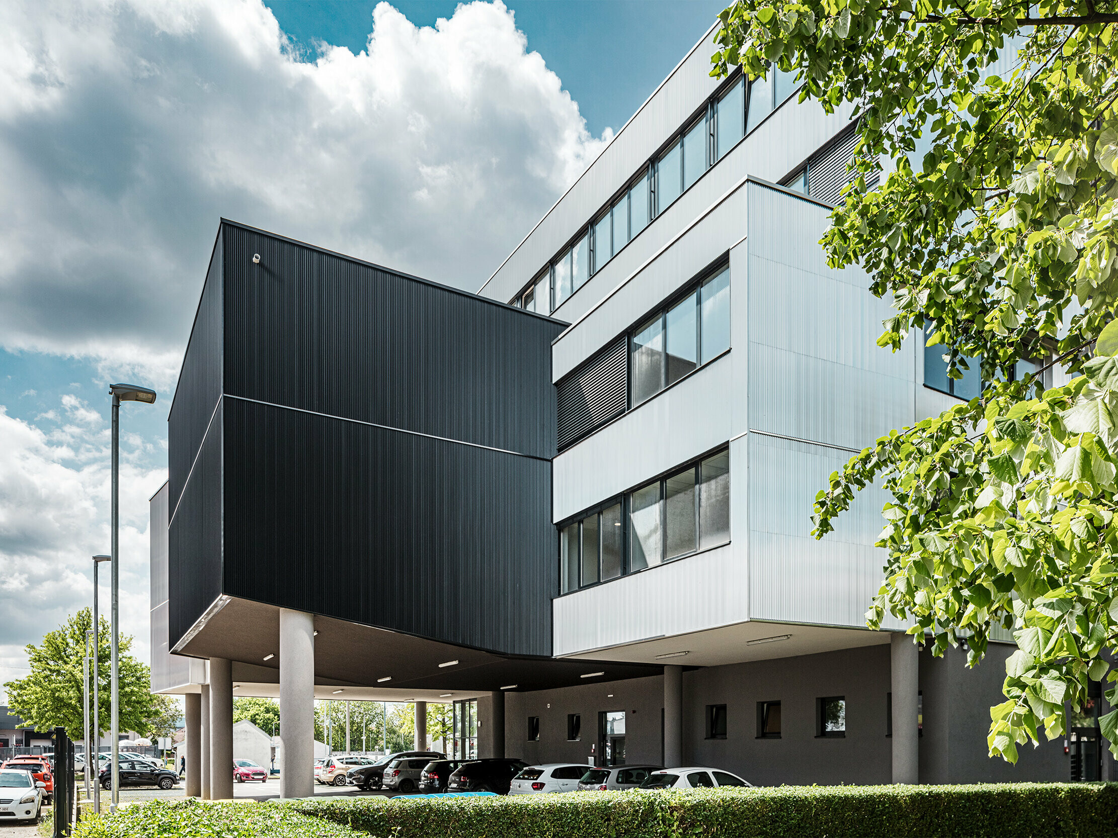 Das moderne Bürogebäude der Musikschule Bjelovar in Kroatien verfügt über eine markante Aluminiumfassade aus PREFA Strangpressprofilen „Zacke”. Die schwarz und silber eloxierten Fassadenflächen setzen klare architektonische Kontraste und verleihen dem Gebäude Charakter und Tiefe. Die senkrecht verlegten Profile erzeugen eine elegante Struktur mit spannender Licht- und Schattenwirkung. Dank der robusten, korrosionsbeständigen Aluminiumoberfläche sind die Fassadenelemente besonders langlebig und pflegeleicht. Die verdeckte Befestigung sorgt für ein gleichmäßiges, hochwertiges Erscheinungsbild. Diese vorgehängte, hinterlüftete PREFA-Fassade vereint Design, Technik und Funktionalität.