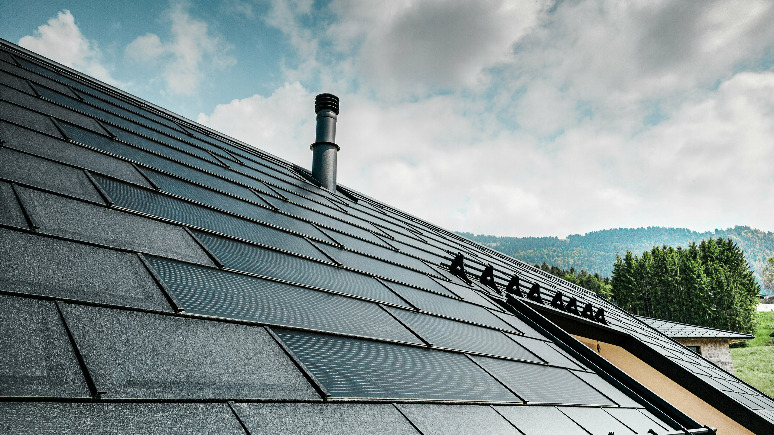 Detailansicht der PREFA Solardachplatte kombiniert mit der bewährten PREFA Dachplatte R.16 in der Farbe P.10 Schwarz auf einem Ökohaus in Egg, Österreich. Die integrierten Photovoltaikmodule zeigen die nahtlose Verbindung von erneuerbarer Energie und anspruchsvollem Dachdesign. Die schwarzen Dachplatten R.16 mit dem Schneeschutzsystem runden die ästhetische Dachoberfläche ab sorgen zudem für Sicherheit.