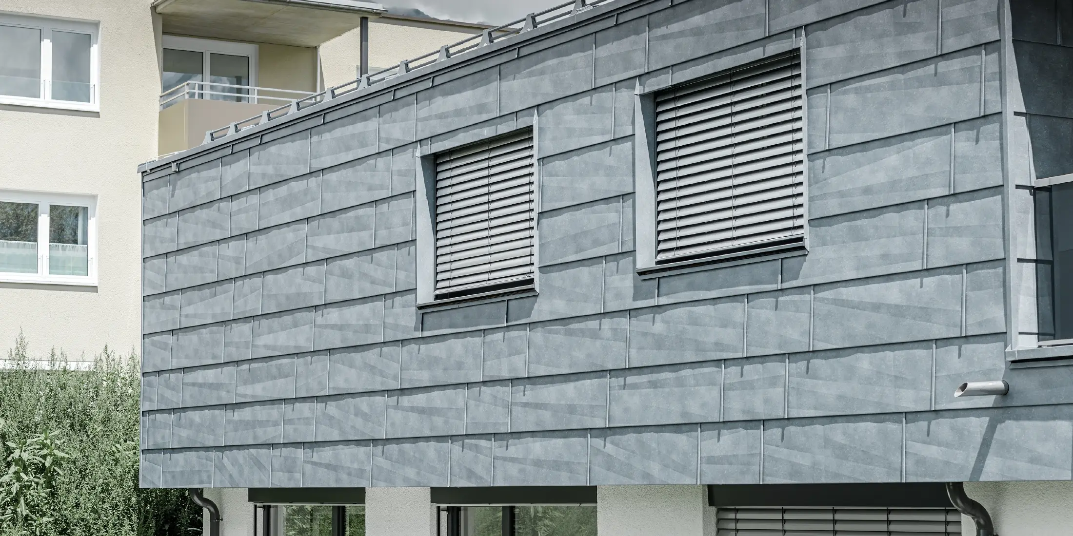 Fassadenfläche mit zwei Fenstern; Die Fassade ist mit dem PREFA Fassadenpanel FX.12 in Steingrau bekleidet.