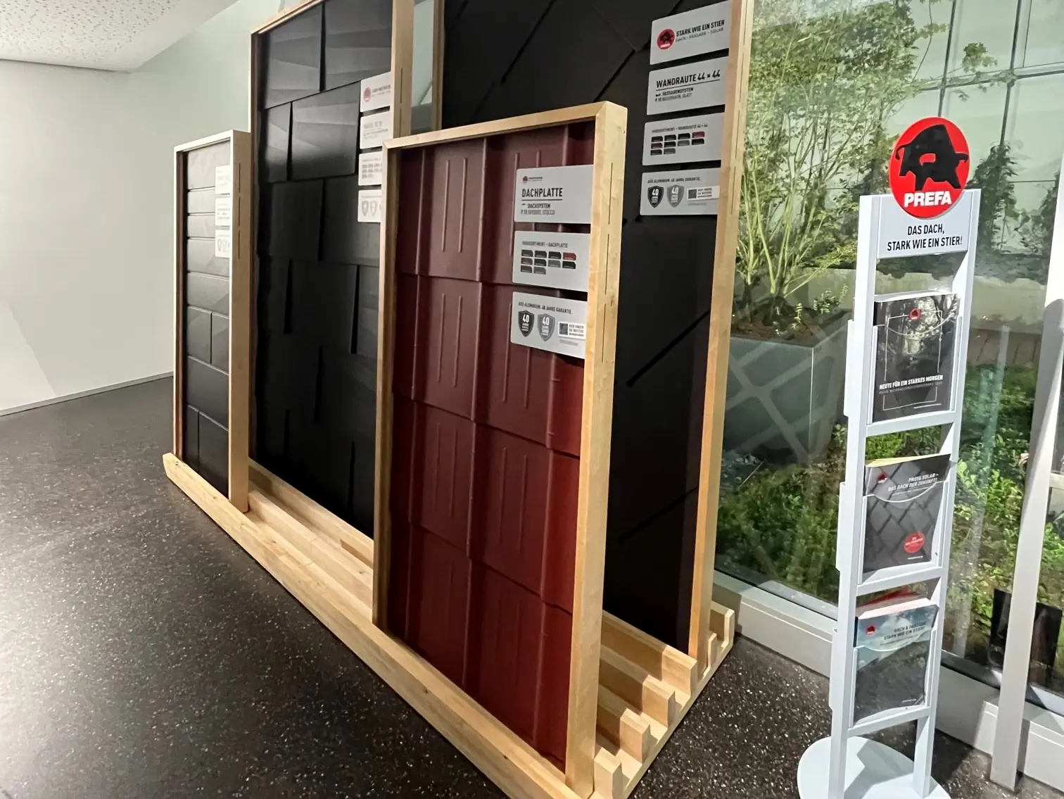PREFA Showroom im Dachzentrum Haberhauer, Amstetten (NÖ), in dem verschiedene Dach- und Fassadenplatten präsentiert werden. Die Ausstellung zeigt unterschiedliche PREFA Produkte, darunter Dachplatten und Wandplatten in diversen Farben und Ausführungen, montiert auf großen, hölzernen Präsentationswänden. Daneben steht ein Prospektständer mit Informationsmaterialien zu den PREFA-Produkten.