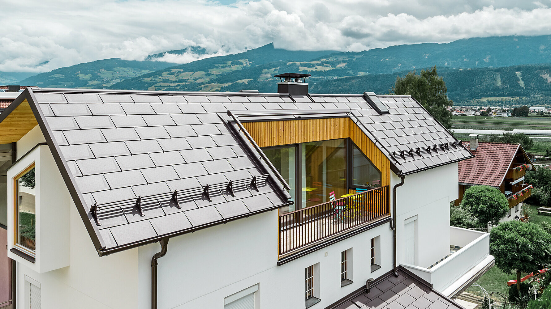 Wohnhaus eingedeckt mit der Aluminium Dachplatte R.16 in Nussbraun von PREFA mit großem Balkon und heller Putzfassade.