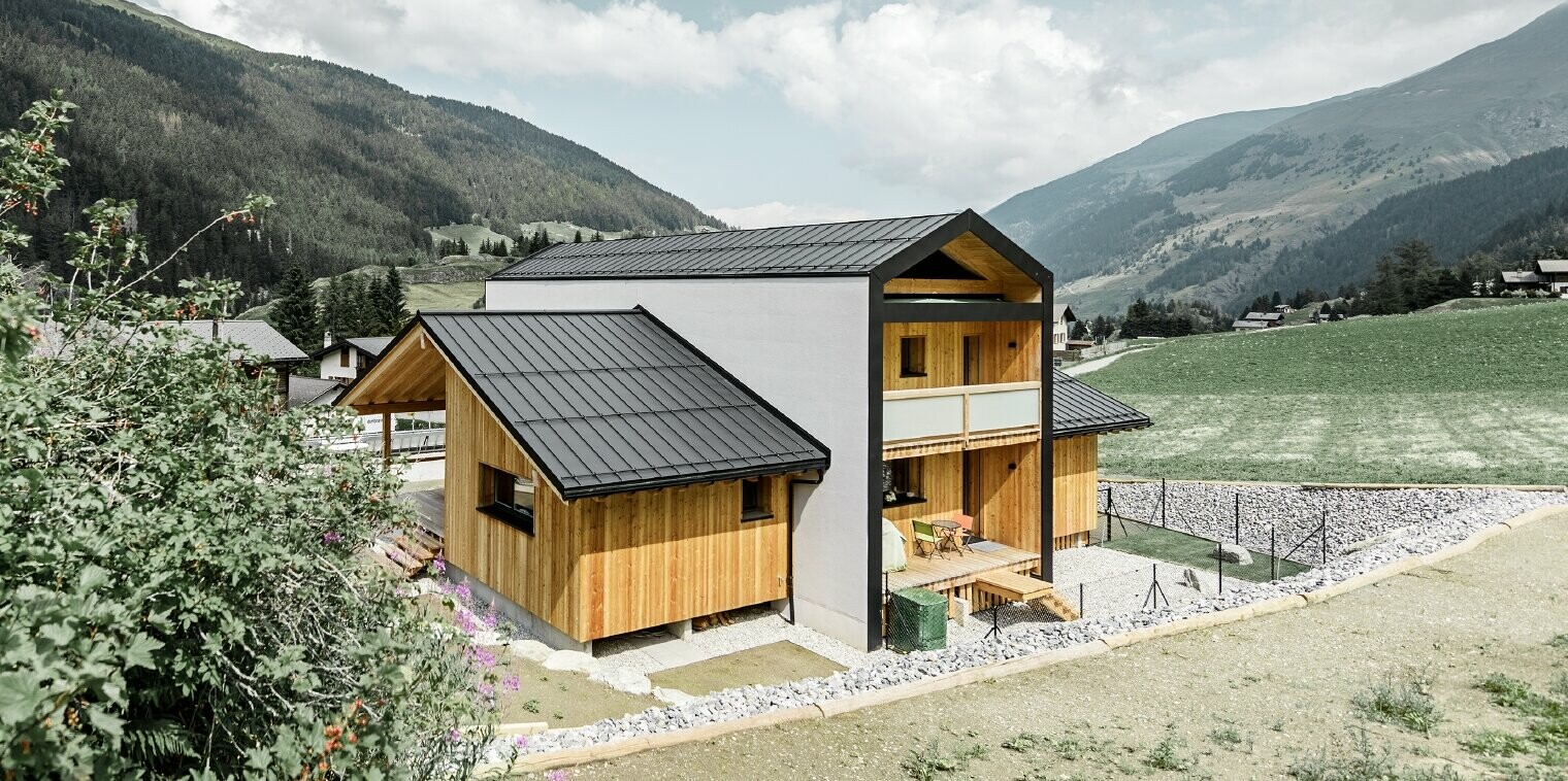 Dieses Einfamilienhaus wirkt, als wären 2 Häuser im 90° Winkel übereinander gestellt worden. Das Dach ist mit Prefalz in Schwarz und die Fassade zum Teil mit Holz verkleidet.
