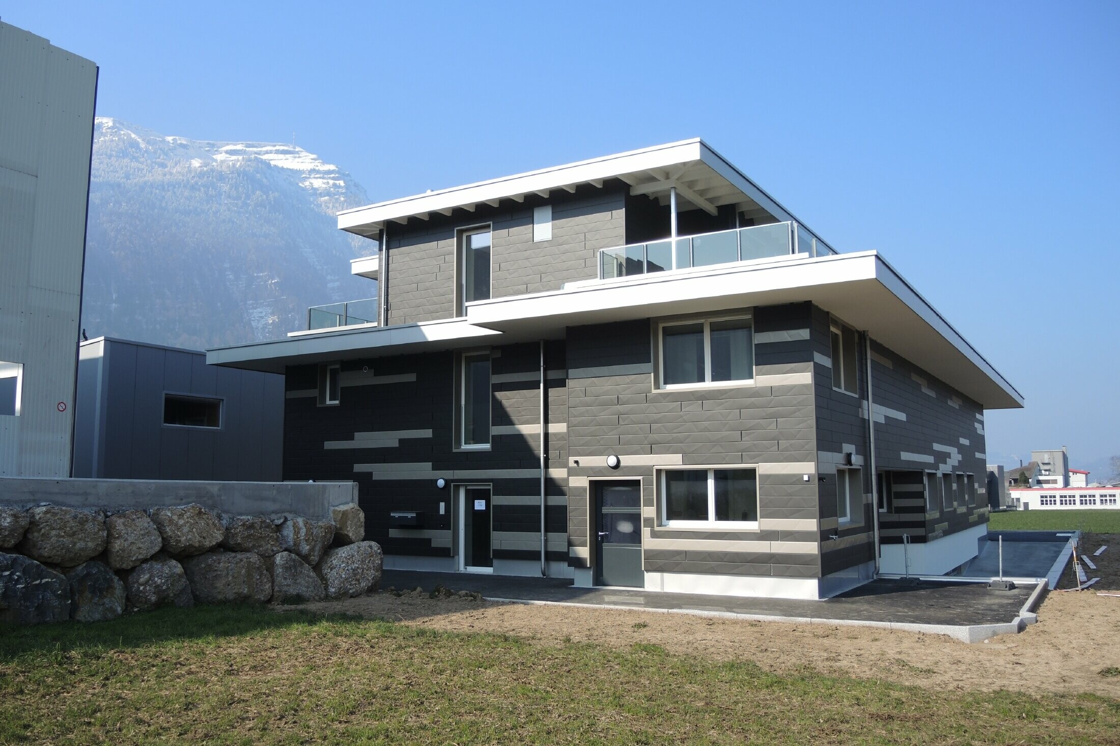 Individuelle Fassadengestaltung mit der vorgehängten hinterlüfteten Alufassade von PREFA. Die Fassade wurde mit den Fassadenpaneelen Siding.X in den Farben schwarzgrau und bronze gestaltet. Die Paneele haben eine geknickte Optik und wirf somit ein interessantes Schattenmuster.