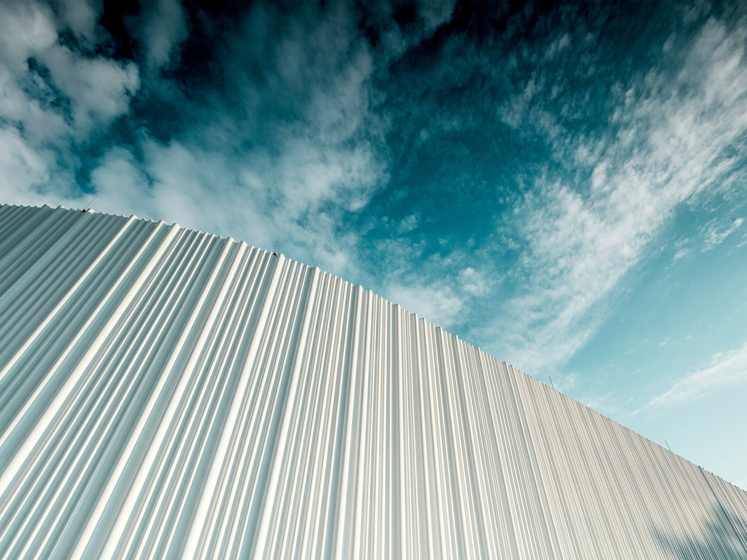 Atemberaubende Architektur mit weißer PREFA Aluminiumfassade im Walter Business-Park bei Wien. Die Fassade aus maßgefertigten Individualprofilen erzeugt durch ihren fließenden Wellencharakter ein faszinierendes Spiel aus Licht und Schatten. Drei unterschiedliche Profilformen sorgen für eine außergewöhnliche Tiefenwirkung und verleihen dem Gebäude eine stilistisch klare und zugleich dynamische Optik. Die langlebige, witterungsbeständige PREFA Oberfläche kombiniert moderne Ästhetik mit funktionaler Perfektion – ein echtes Highlight zeitgenössischer Fassadengestaltung, das architektonische Qualität und technische Raffinesse sichtbar macht.