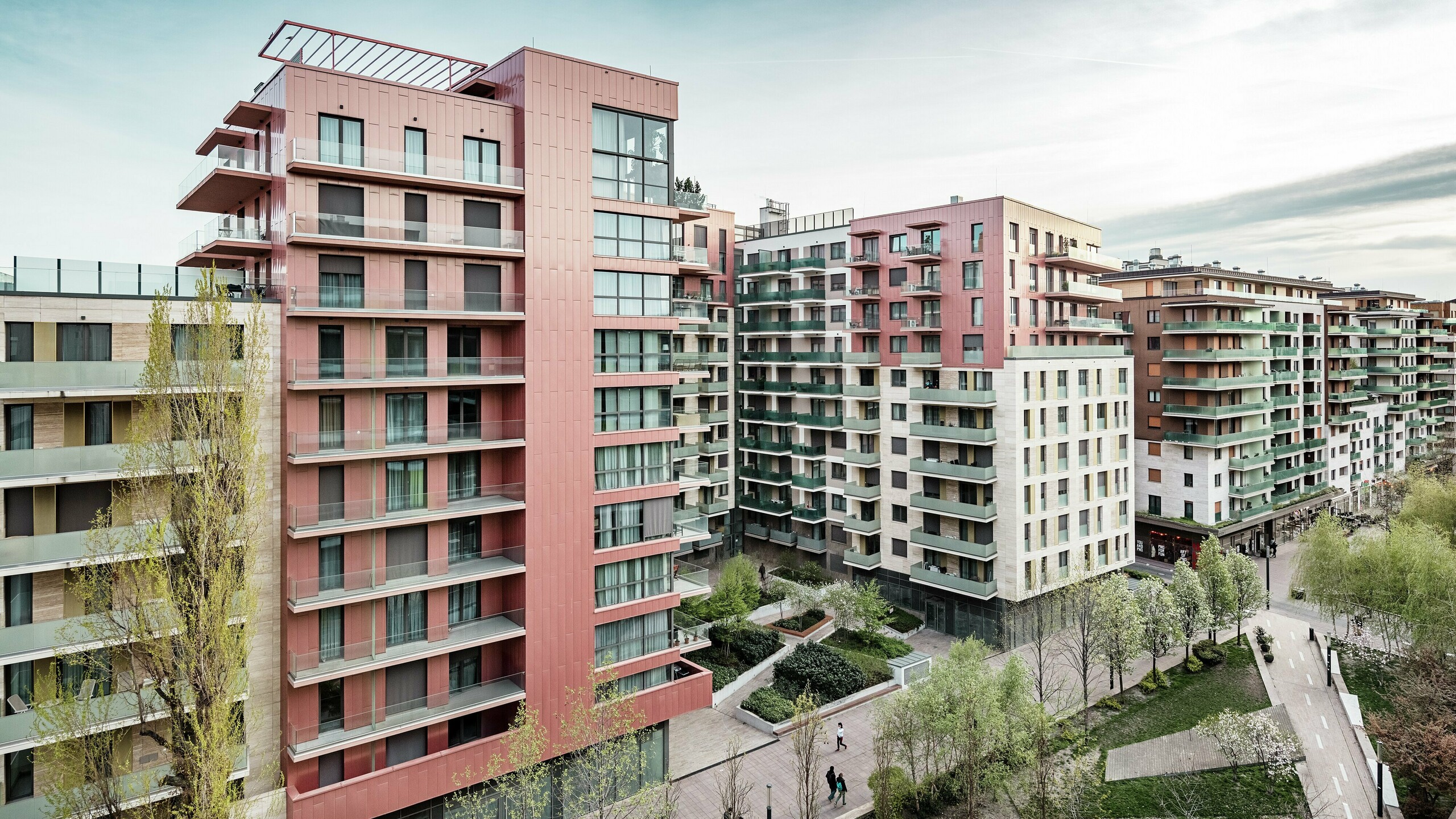 Panoramaaufnahme des Grand Corvin Wohnkomplexes im neugestalteten Corvin-Viertels in Budapest. Die markanten Gebäudeteile sind mit über 800 m² PREFA Siding Fassadenpaneelen in vertikaler Verlegung und Sonderfarbe Lachsmetallic versehen. Die langlebige Aluminiumverkleidung setzt architektonische Highlights, fügt sich harmonisch in die urbane Struktur ein und unterstreicht den hochwertigen, zeitgemäßen Charakter der neuen Wohnanlage entlang der Corvin-Promenade.