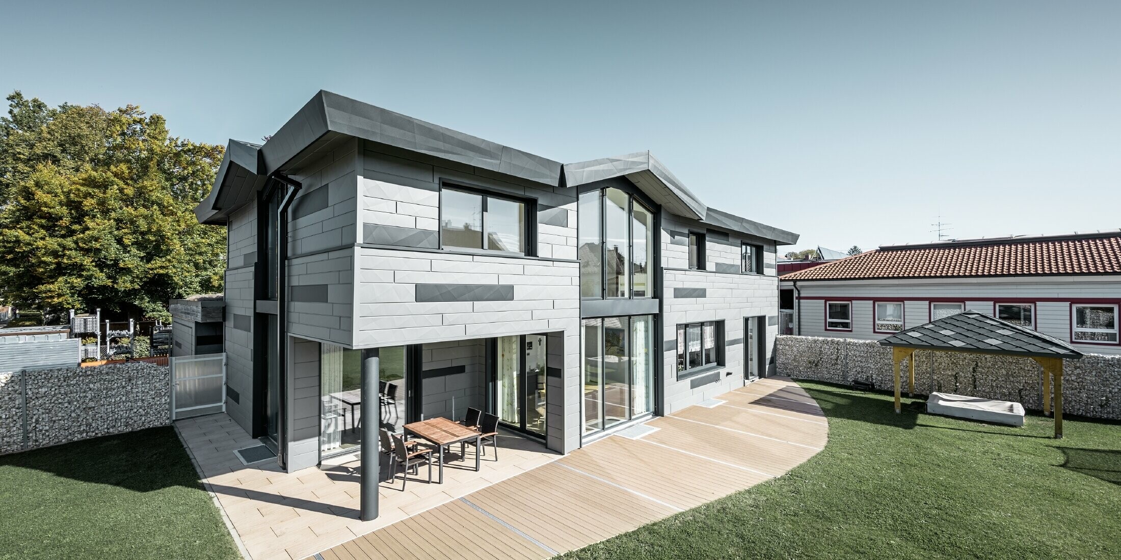 Das moderne Einfamilienhaus in Türkheim präsentiert die PREFA Fassadenpaneelen FX.12 in den Farben P.10 Hellgrau und Anthrazit. Das Bild zeigt einen Teil vom Garten.